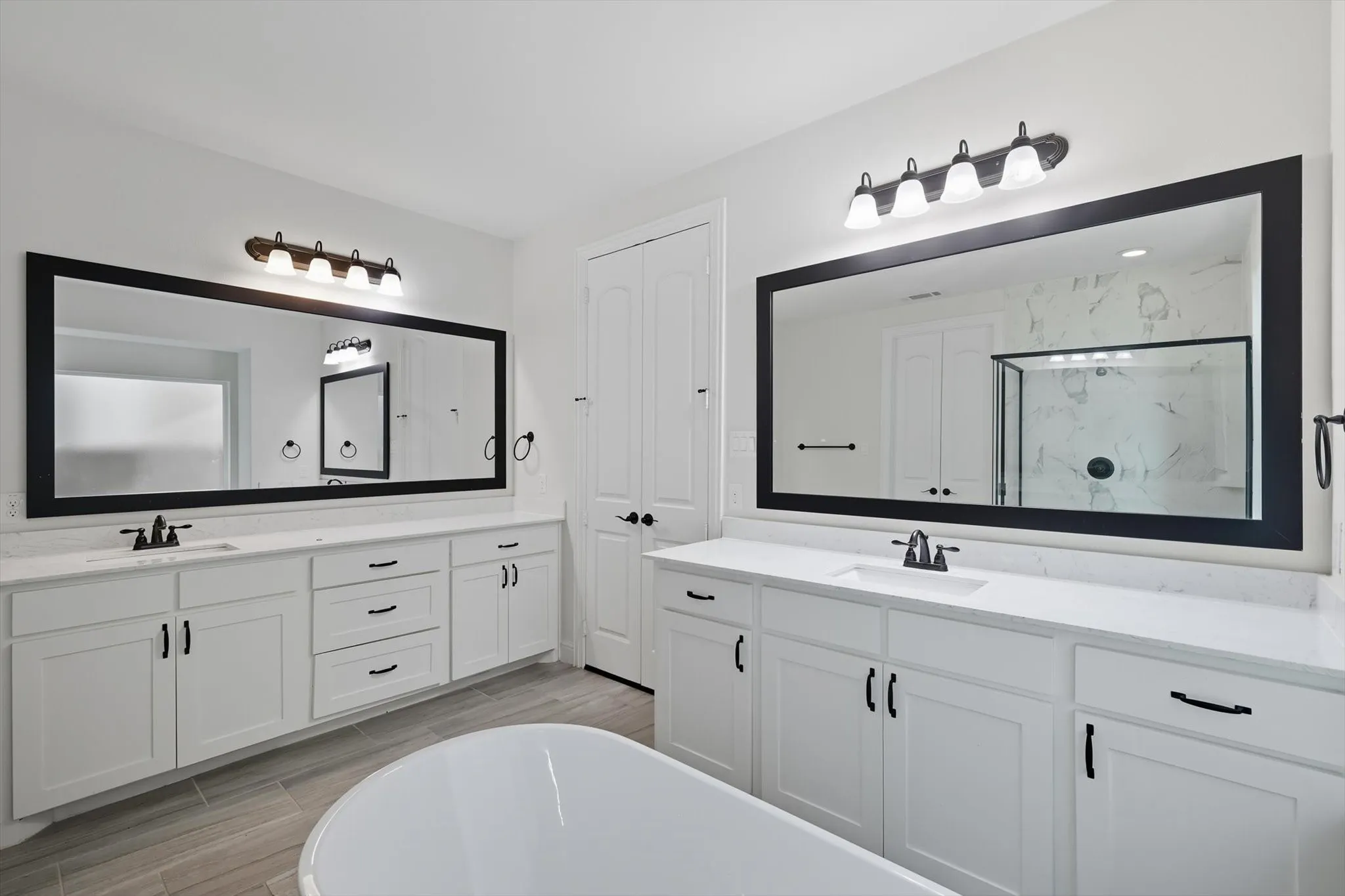 Bathroom with a marble finish shower, a freestanding tub, two vanities, and wood tiled floors