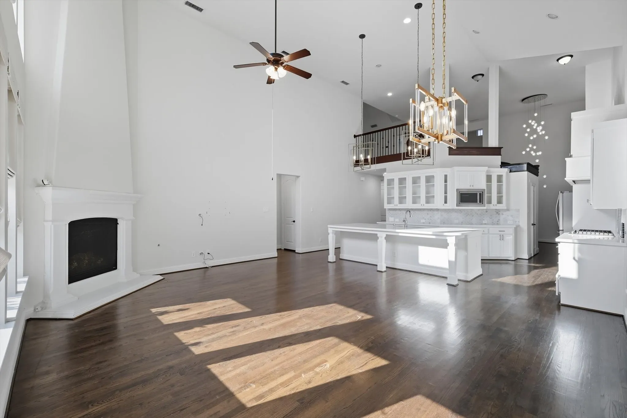 Unfurnished living room featuring a high ceiling, a fireplace, dark wood-type flooring, a chandelier, and a ceiling fan