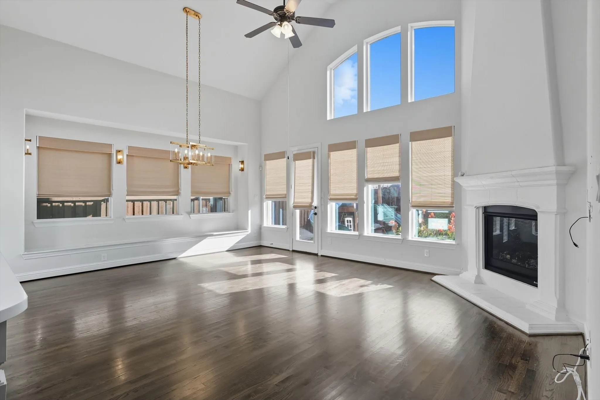 Unfurnished living room with high vaulted ceiling, dark wood finished floors, a glass covered fireplace, a ceiling fan, and a chandelier