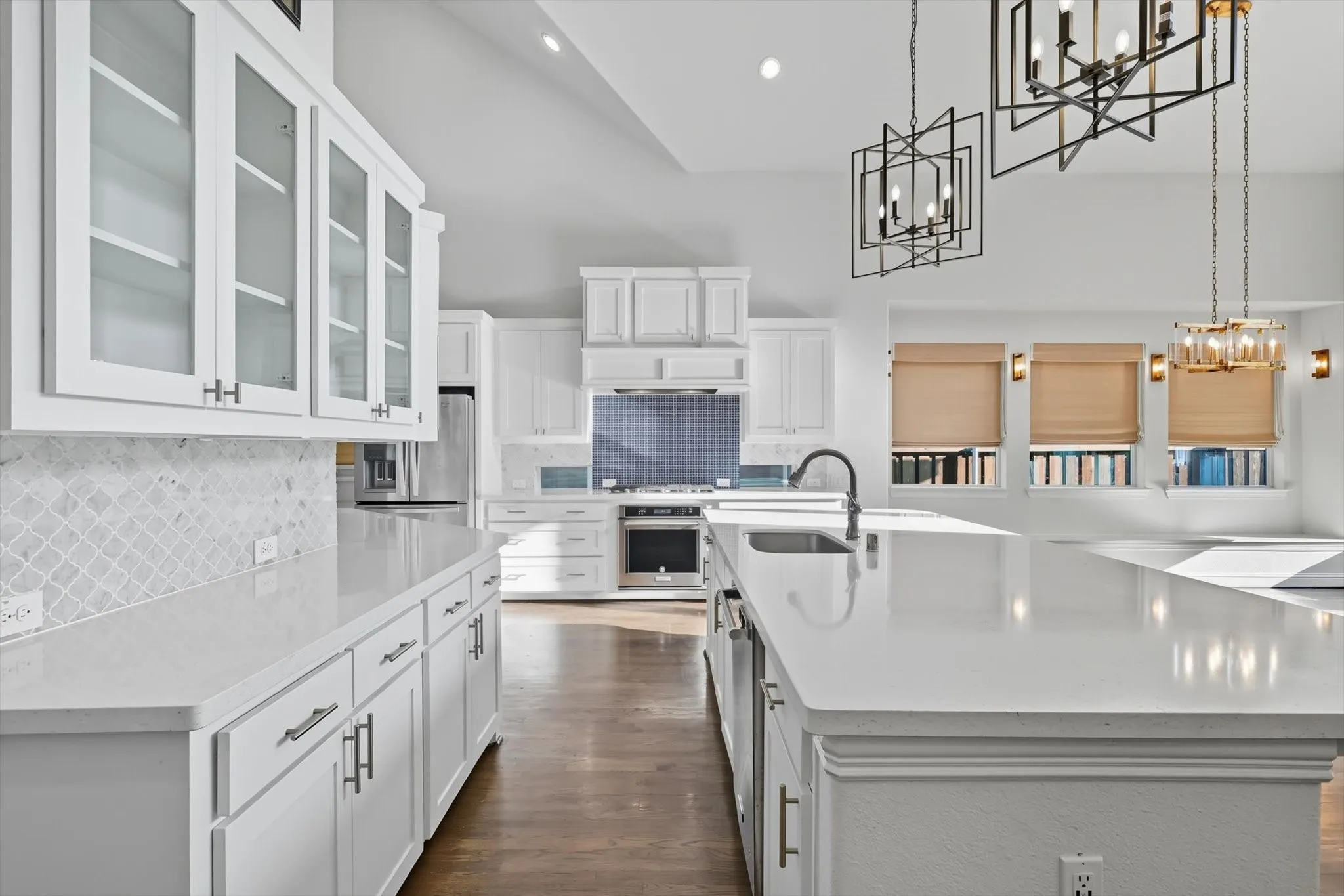 Kitchen with hanging light fixtures, white cabinets, glass insert cabinets, tasteful backsplash, and light stone counters