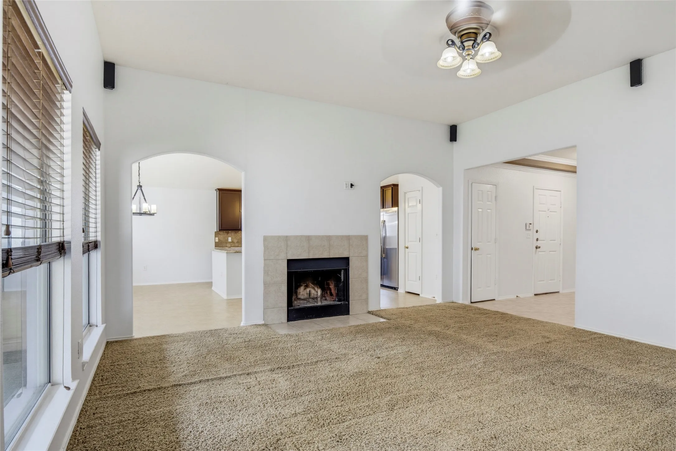 Vaulted ceiling with ceiling fan, tile fireplace surround, arched doorway, and built-in wall speakers
