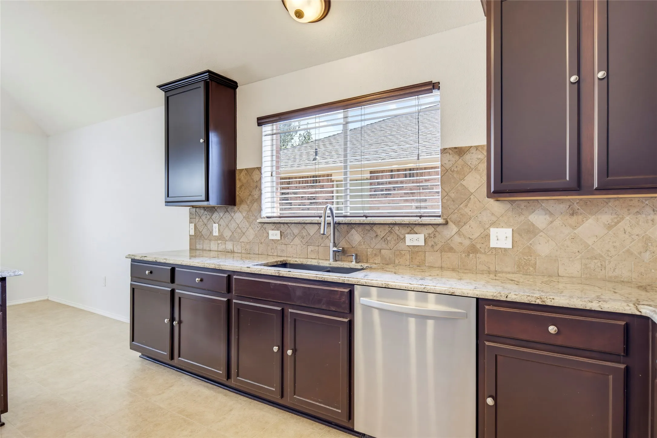 Dark wood cabinetry with brushed nickel hardware, granite countertops, tile backsplash, and stainless steel dishwasher