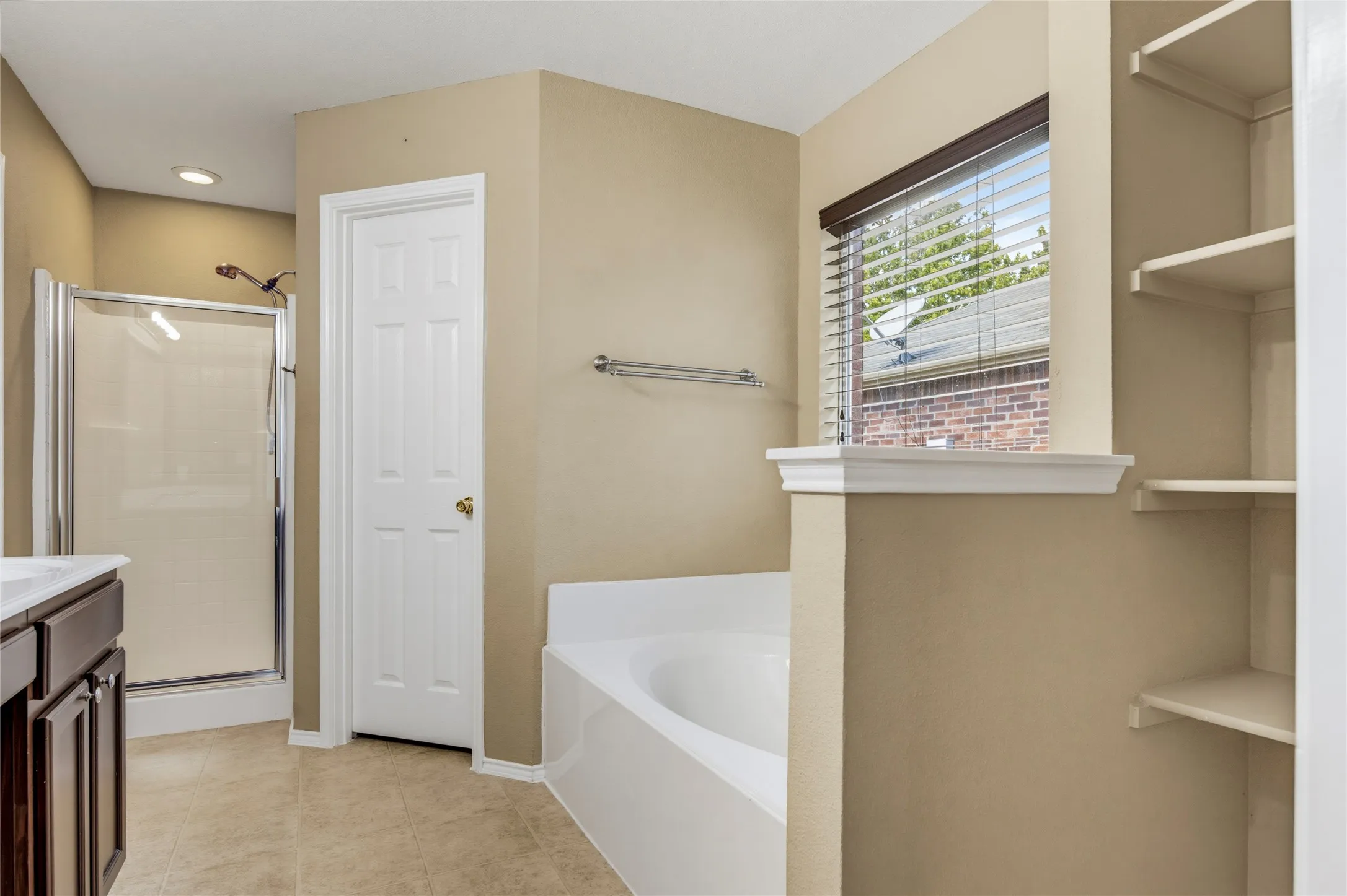 Glass-enclosed shower, soaking tub, built-in shelving, vanity with integrated sink, and tile flooring