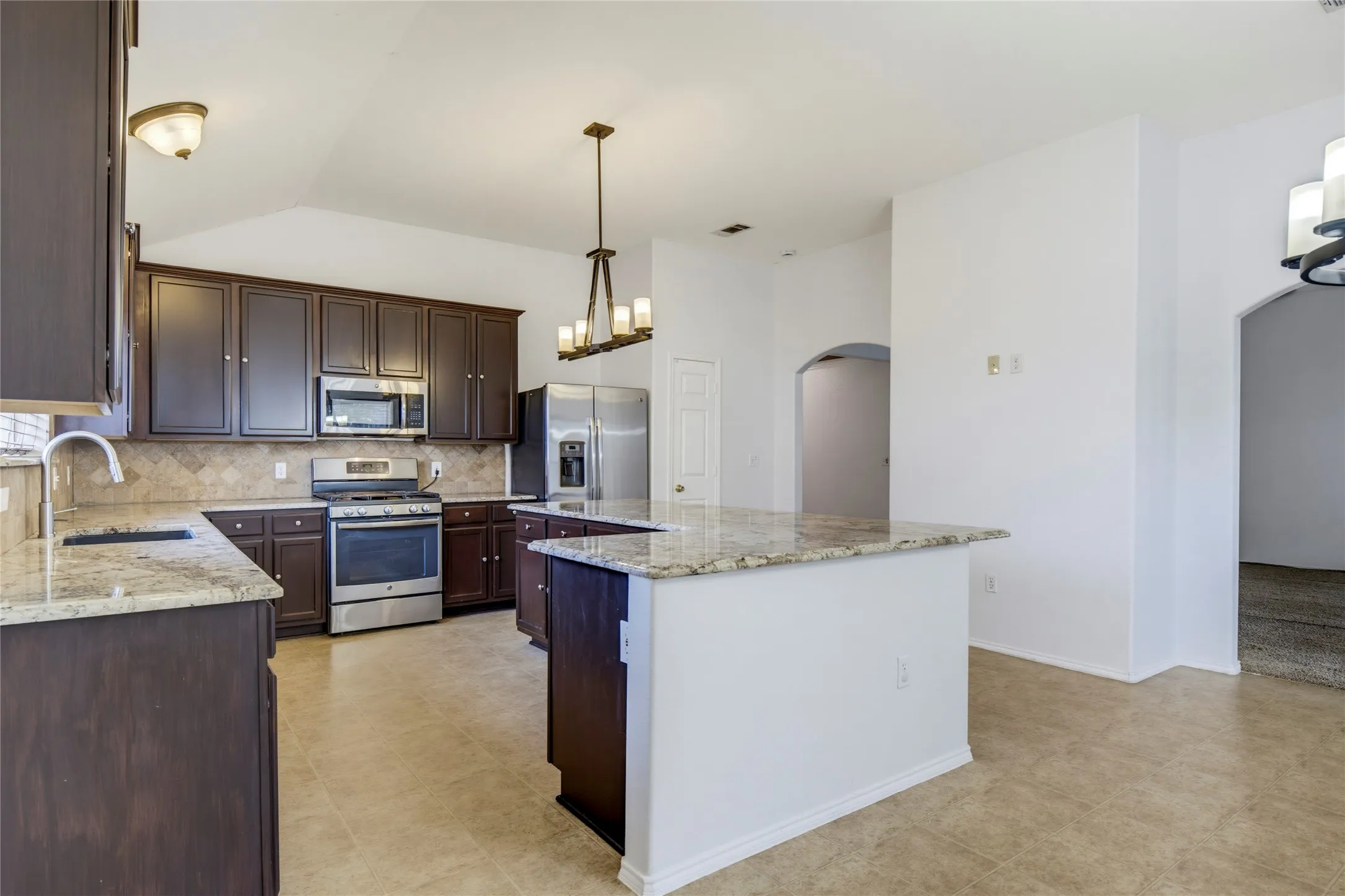 Kitchen featuring dark wood cabinetry, light-toned countertops, stainless steel appliances, and a tiled backsplash