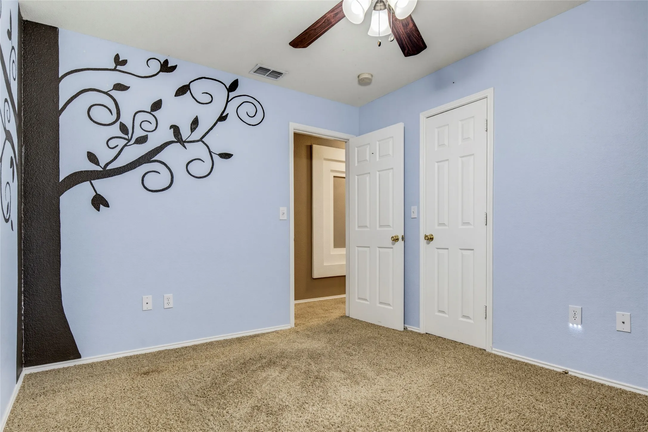 Wall-to-wall carpeting with light blue walls, a ceiling fan with light fixture, and two panel doors with gold-toned hardware
