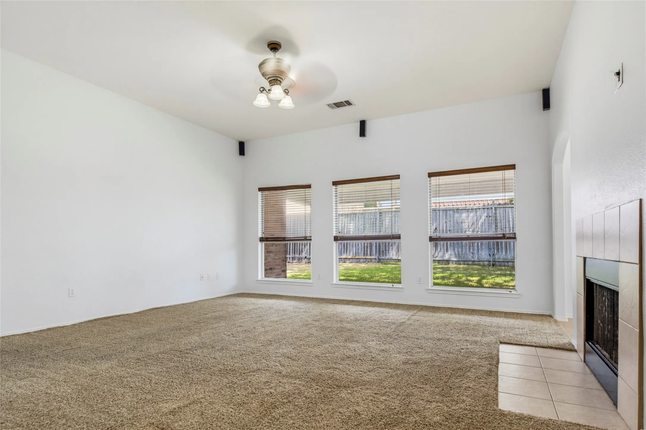 Spacious room featuring three large windows, a ceiling fan, and an integrated fireplace with a tiled hearth