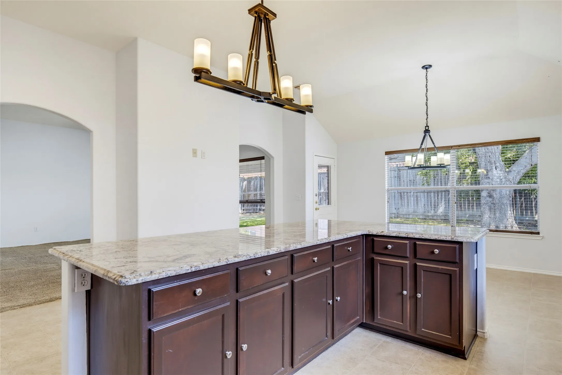 L-shaped island with granite countertop, dark wood cabinetry, and recessed panel doors