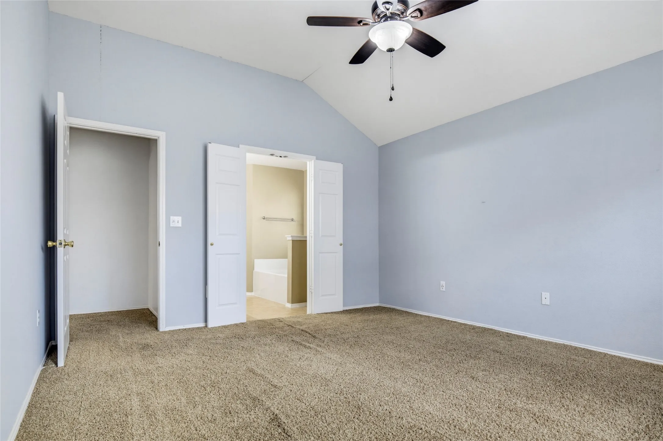 Carpeted room featuring a vaulted ceiling with a ceiling fan, light blue wall paint, and double bi-fold doors
