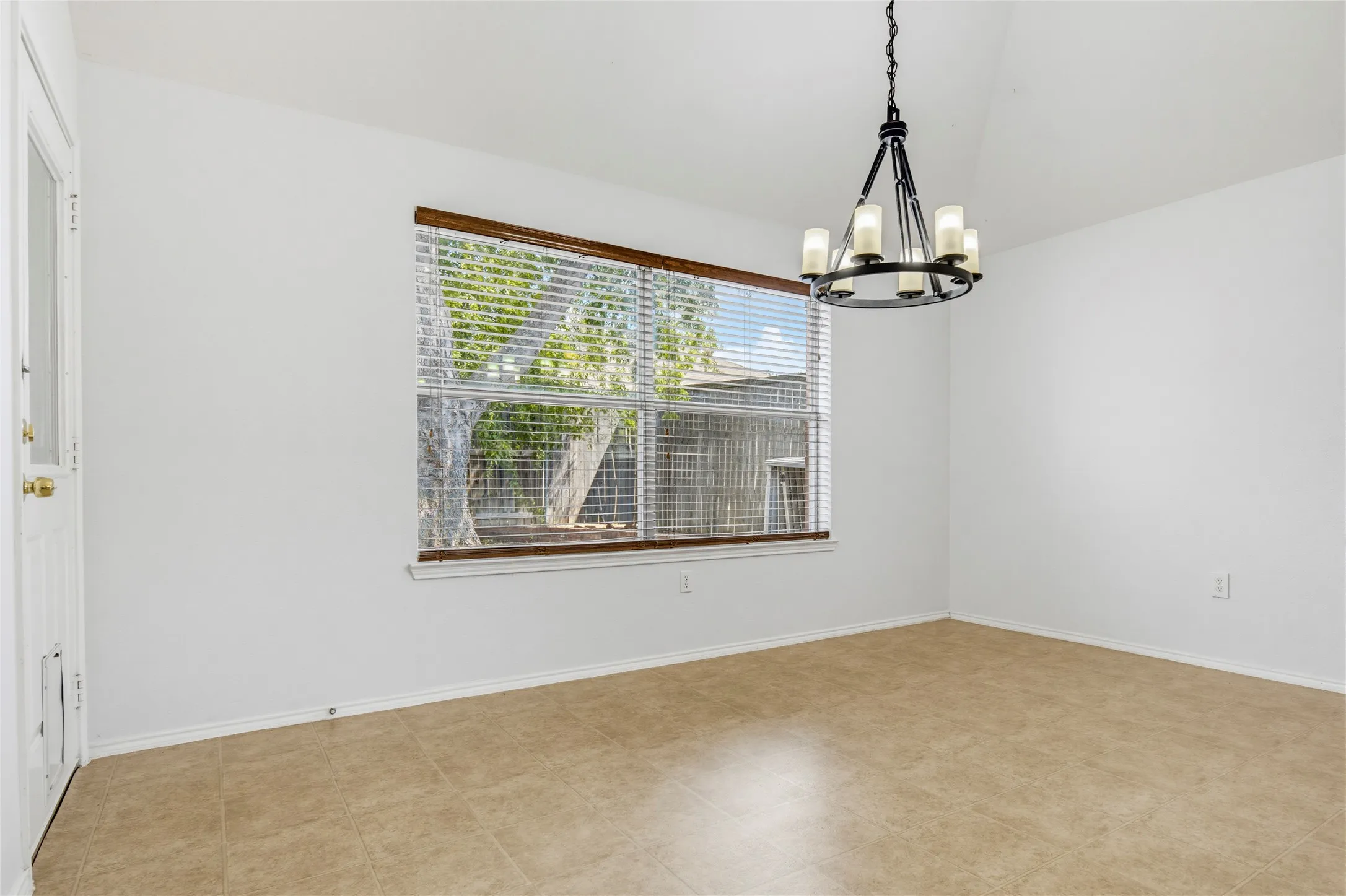Vaulted ceiling with a chandelier, tile flooring, and a window with horizontal blinds