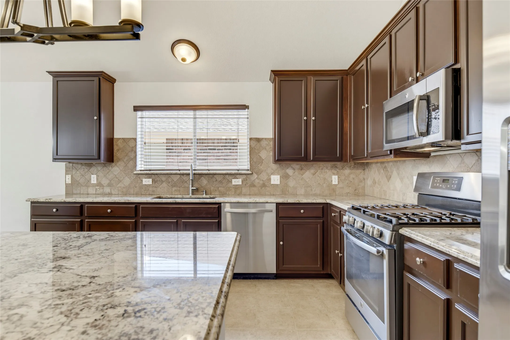Kitchen featuring wood-finish cabinetry, stainless steel appliances, granite countertops, tile backsplash, and a built-in sink