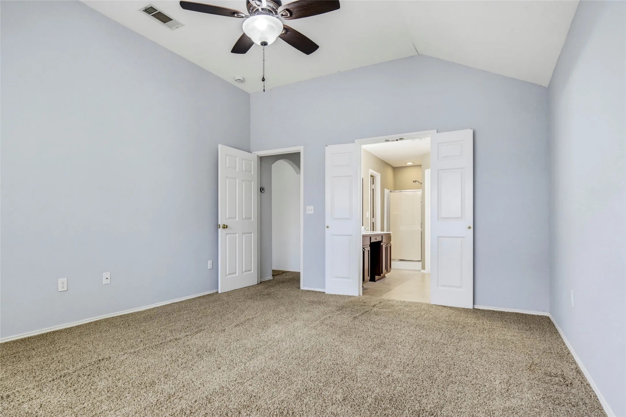 Vaulted ceiling with a ceiling fan, light-colored carpeting, white paneled doors, and an arched entry