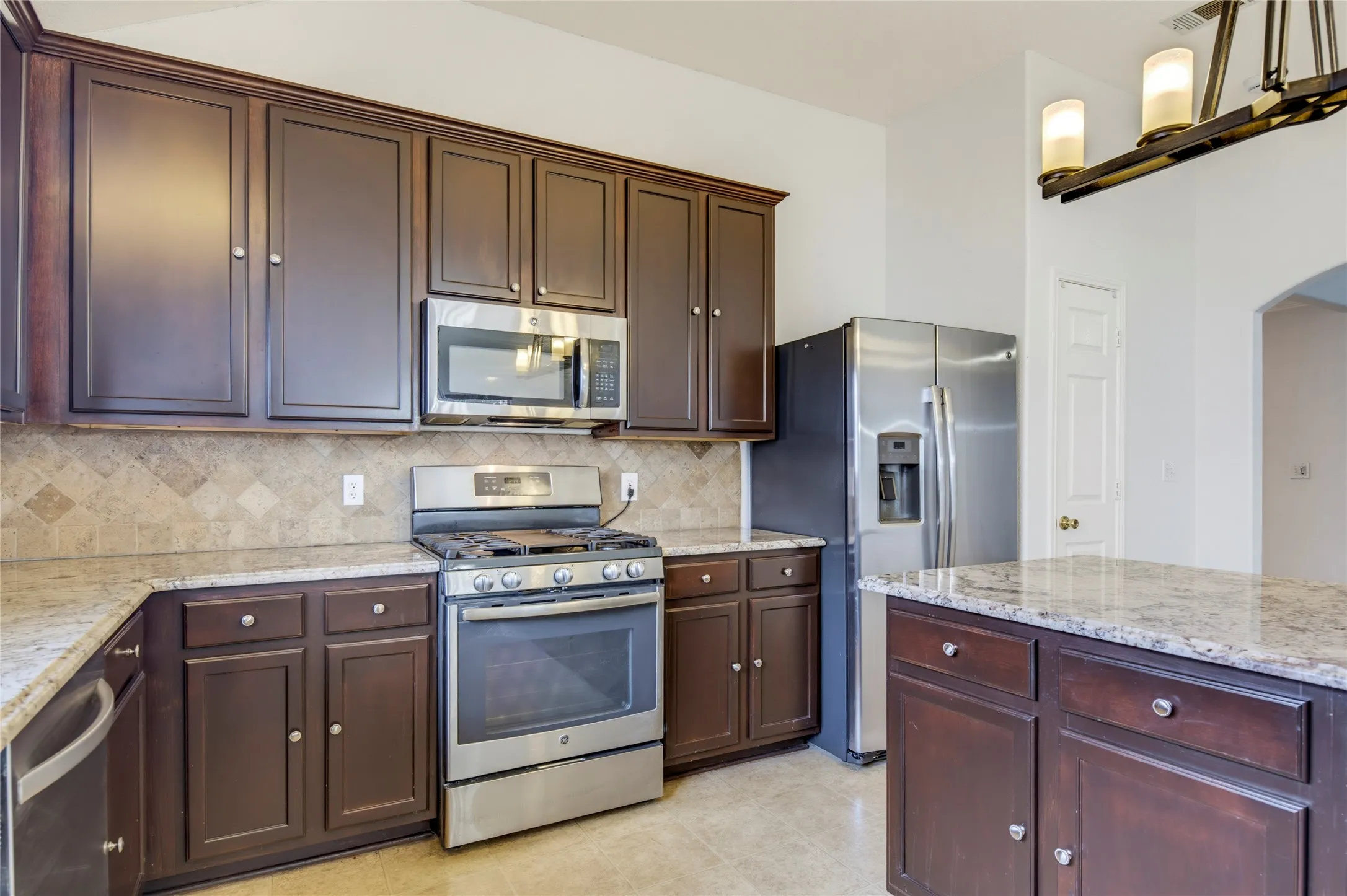 Kitchen featuring dark wood cabinetry, light granite countertops, stainless steel appliances, and a tiled backsplash