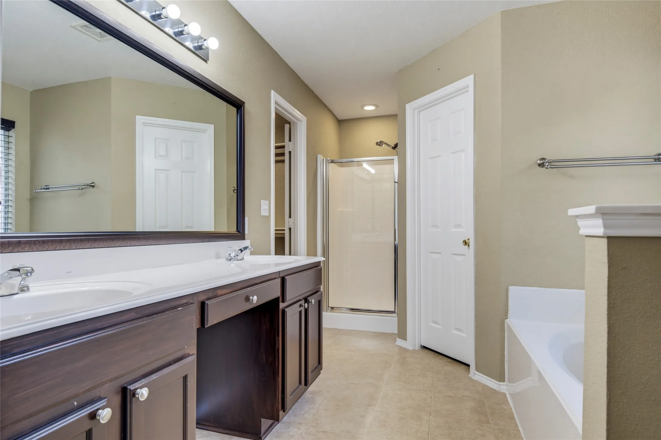 Dual vanity with integrated sinks, dark wood-finish cabinetry, a large framed mirror, and a walk-in shower with a glass enclosure