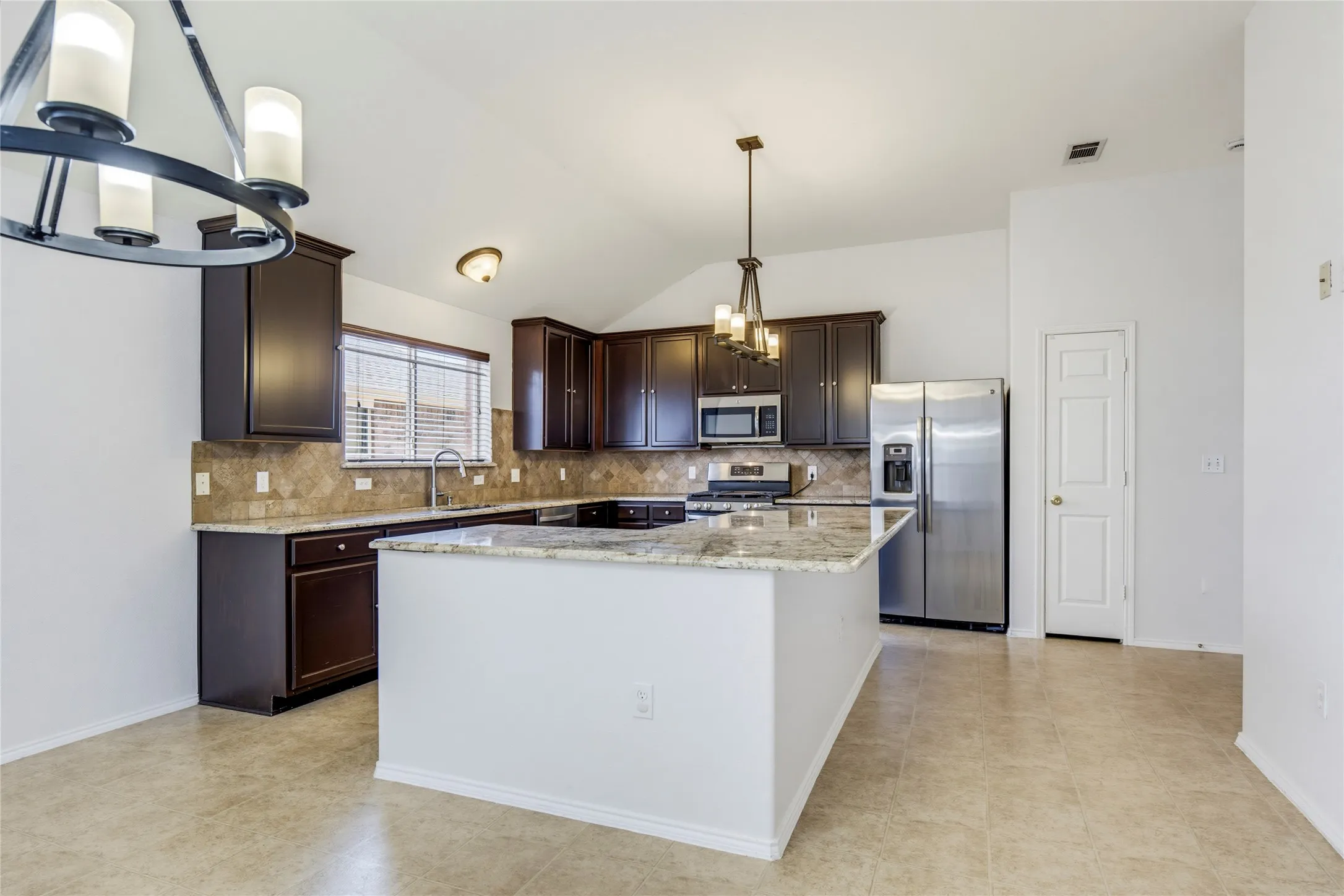 Kitchen featuring dark wood cabinetry, a central island with a light-toned countertop, stainless steel appliances, and a mosaic tile backsplash
