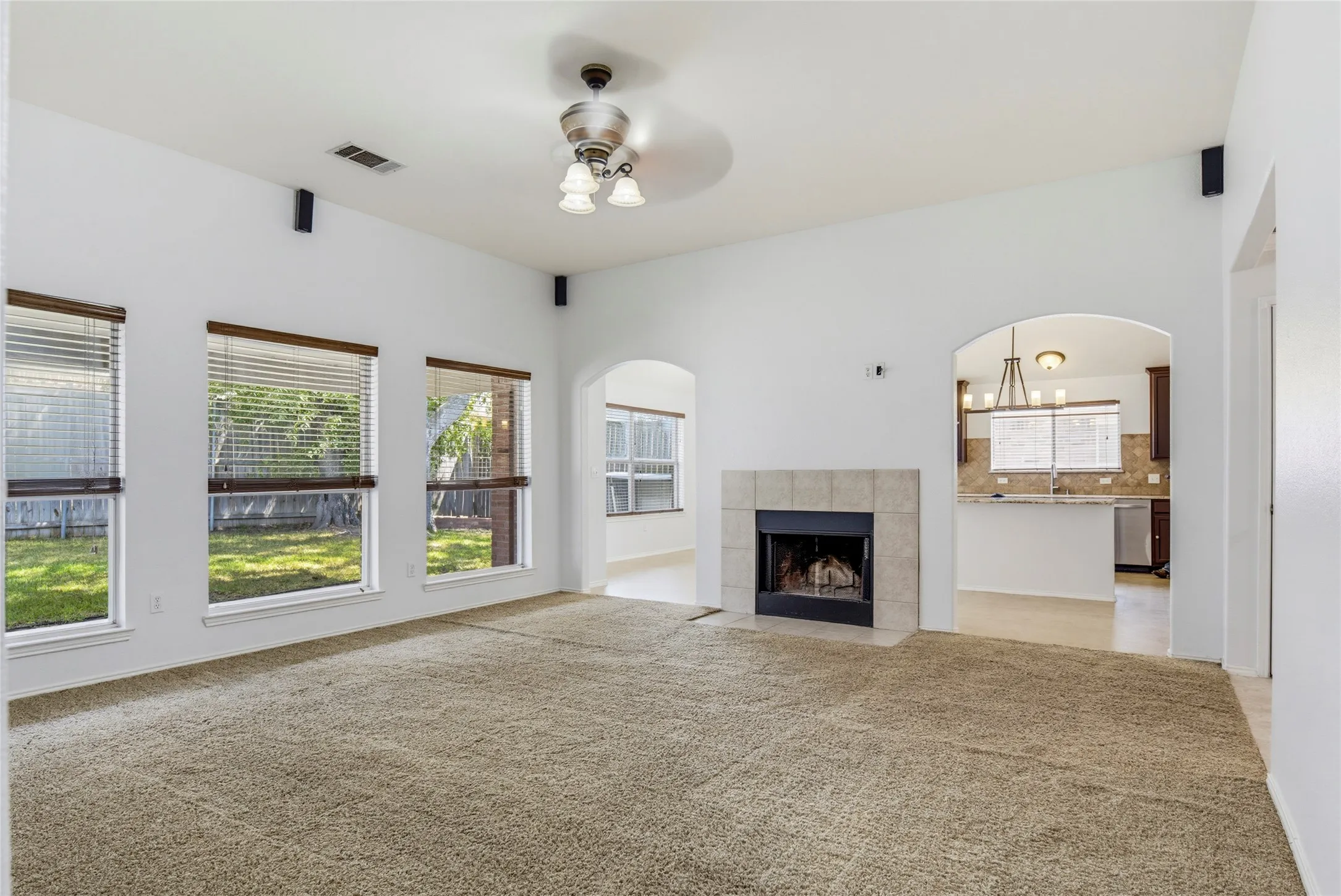 Carpeted living area with a tile-surround fireplace, vaulted ceiling, and multiple windows