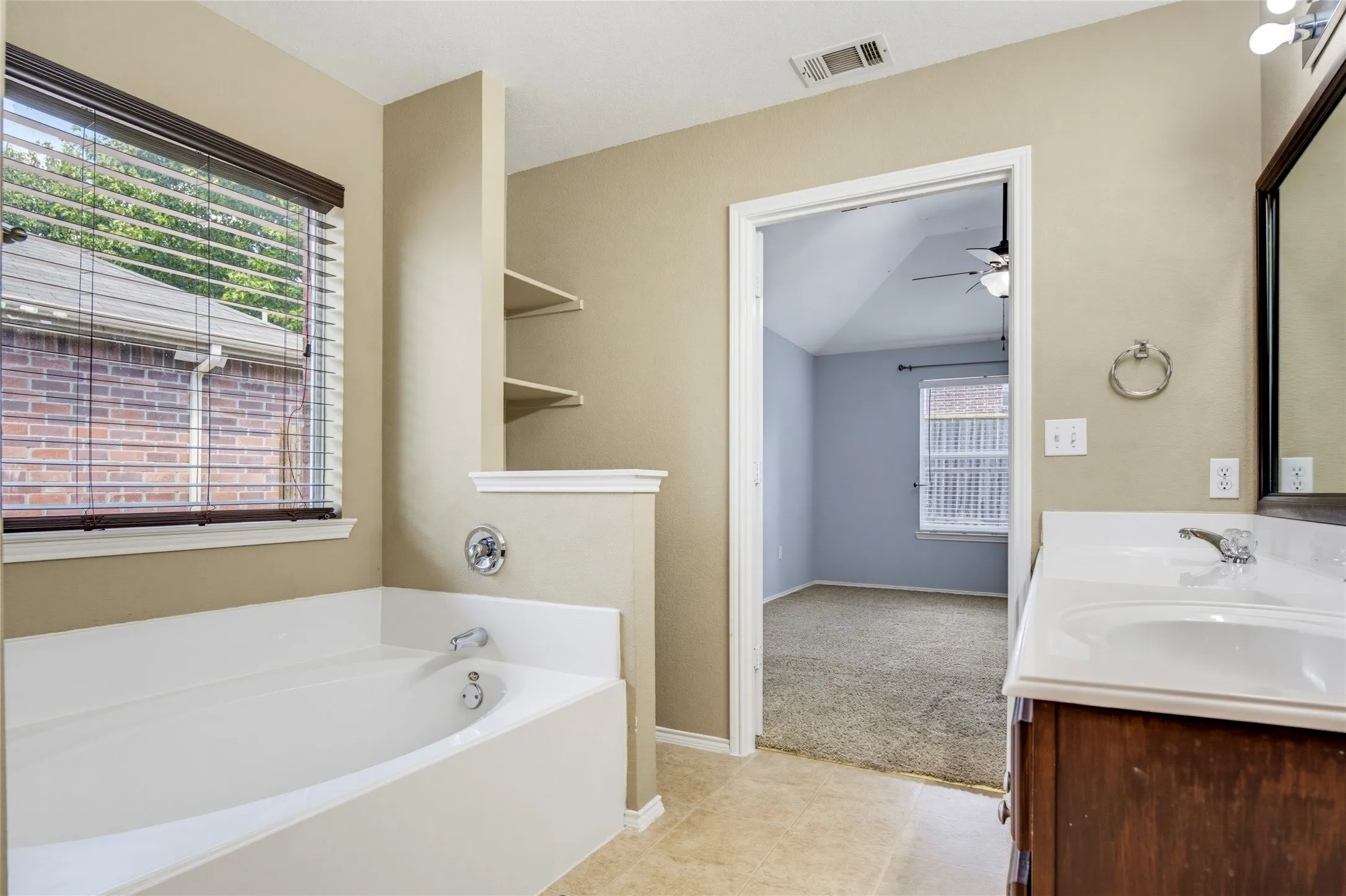Bathtub with chrome fixtures, built-in shelving, wood-finish vanity with white countertop and integrated sink, and an overhead light fixture