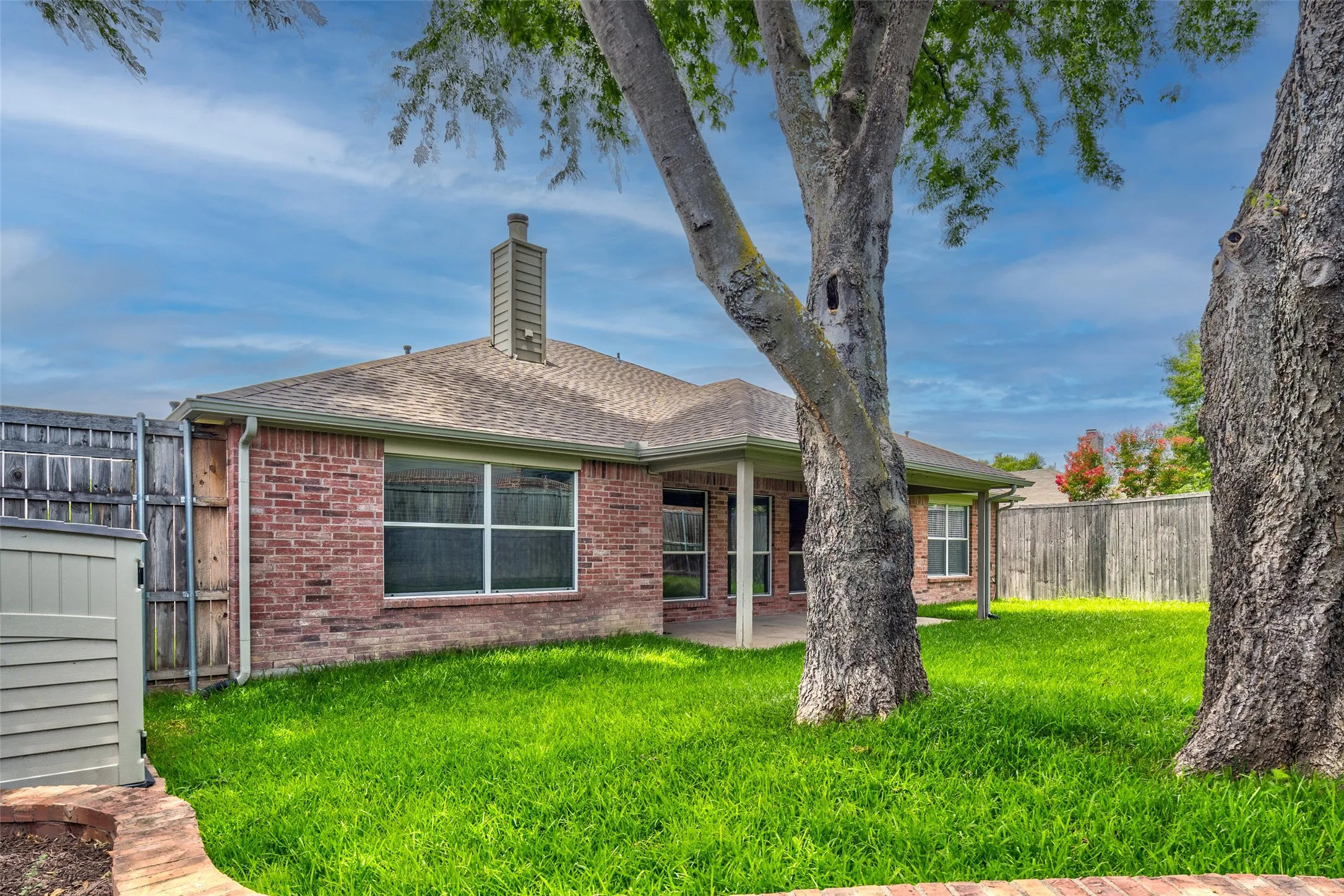 Brick exterior, covered patio, fenced perimeter, mature trees, and chimney