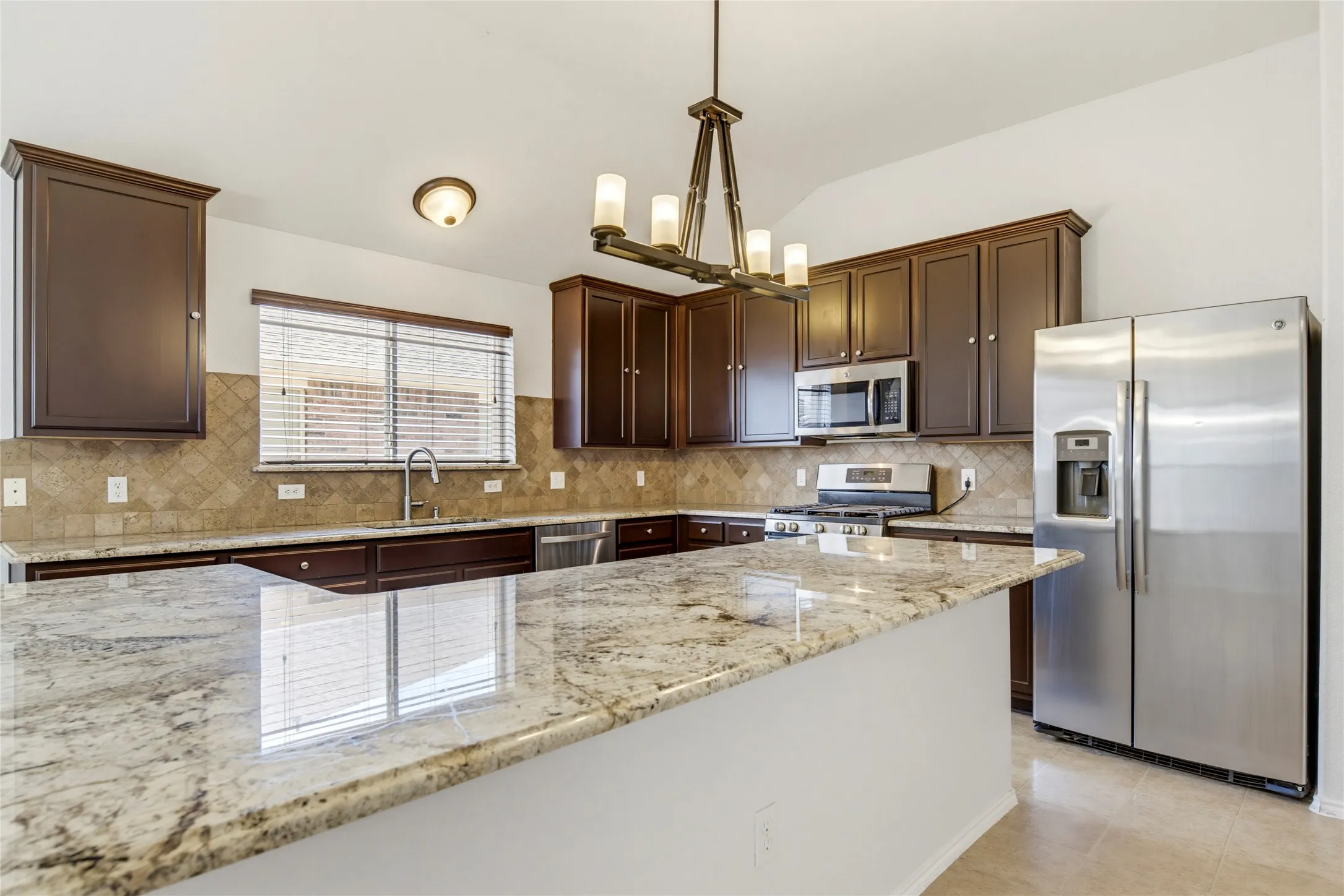 Kitchen featuring a large island with stone countertop, stainless steel appliances, dark wood cabinetry, and a tile backsplash