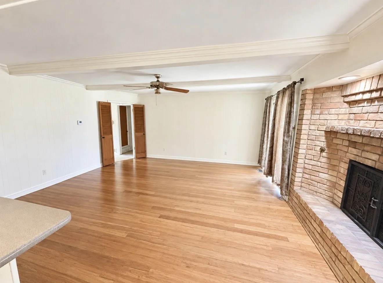Wood-finish flooring, brick fireplace with hearth, and ceiling beams