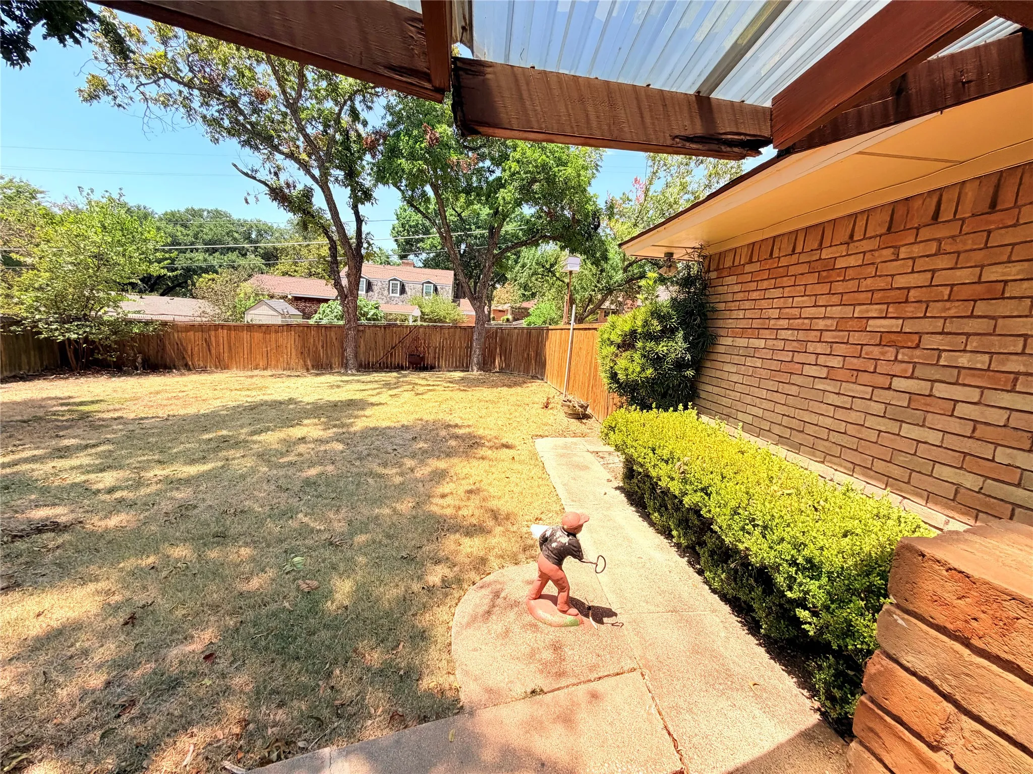 Expansive backyard featuring a wood privacy fence, mature trees, a concrete walkway, and brick exterior