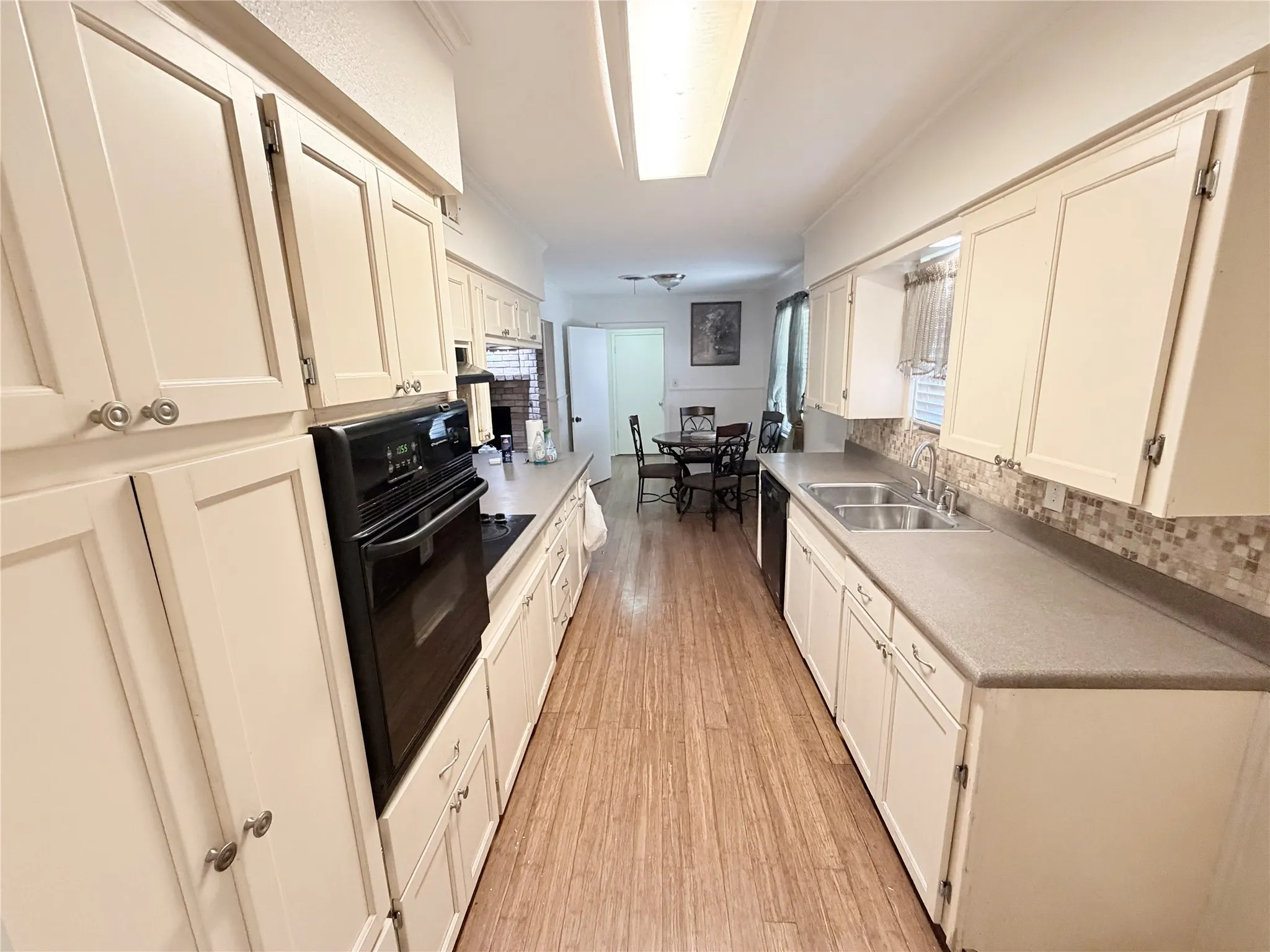 Galley kitchen featuring wood-finish flooring, white cabinetry, dark countertops, and a tile backsplash