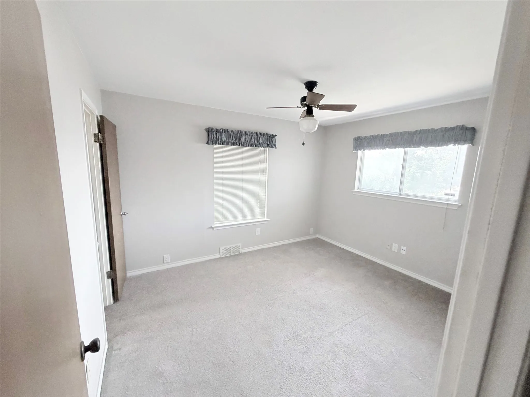 Neutral tone wall paint with soft carpet flooring, multiple windows, and a ceiling fan with integrated lighting
