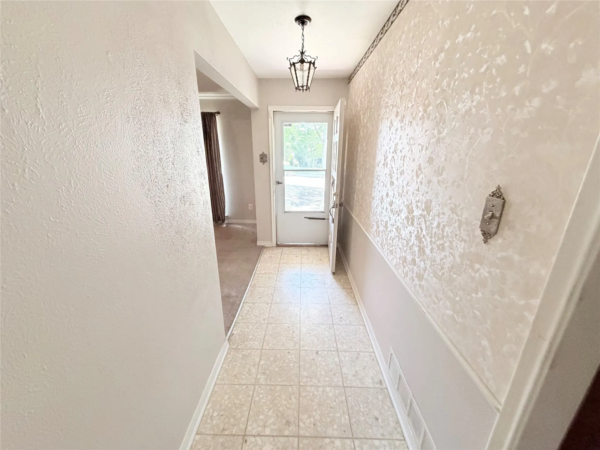Foyer featuring tile flooring, textured wallpaper, and a decorative ceiling light fixture