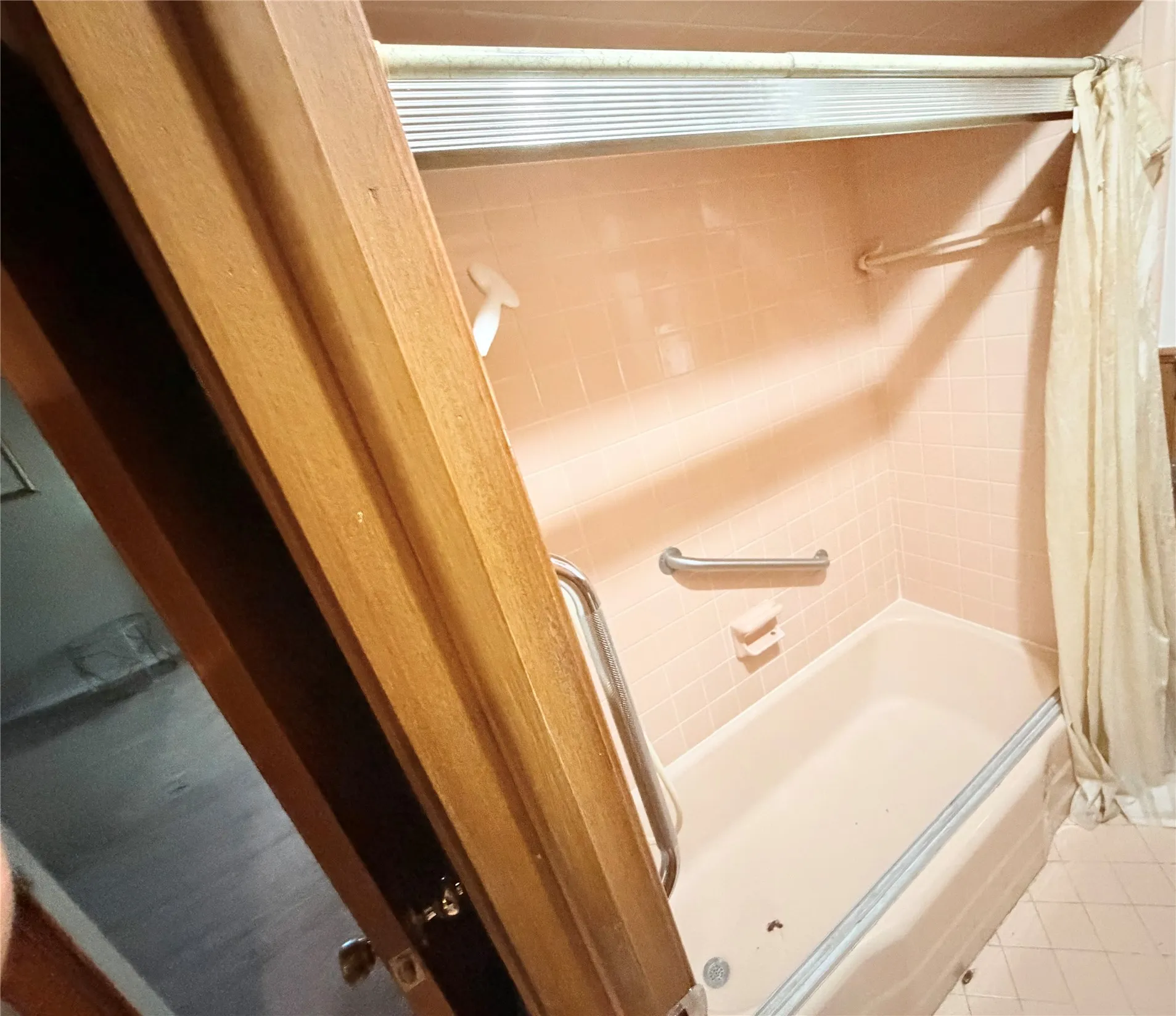 Built-in bathtub with a tile surround, mounted grab bars, and a shower curtain rod