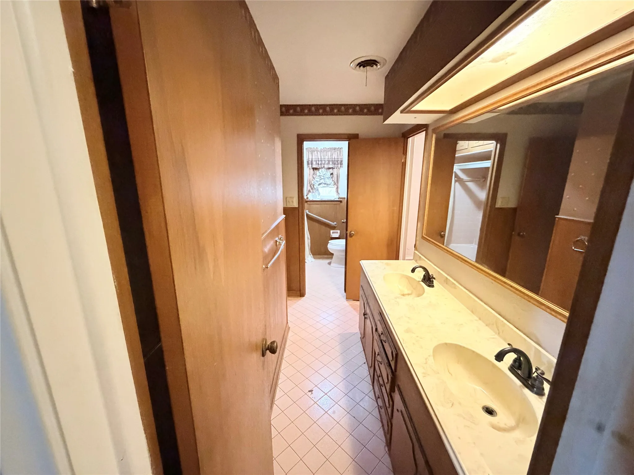 Double vanity with dual sinks, overhead lighting, wood-finish cabinetry, and a large mirror
