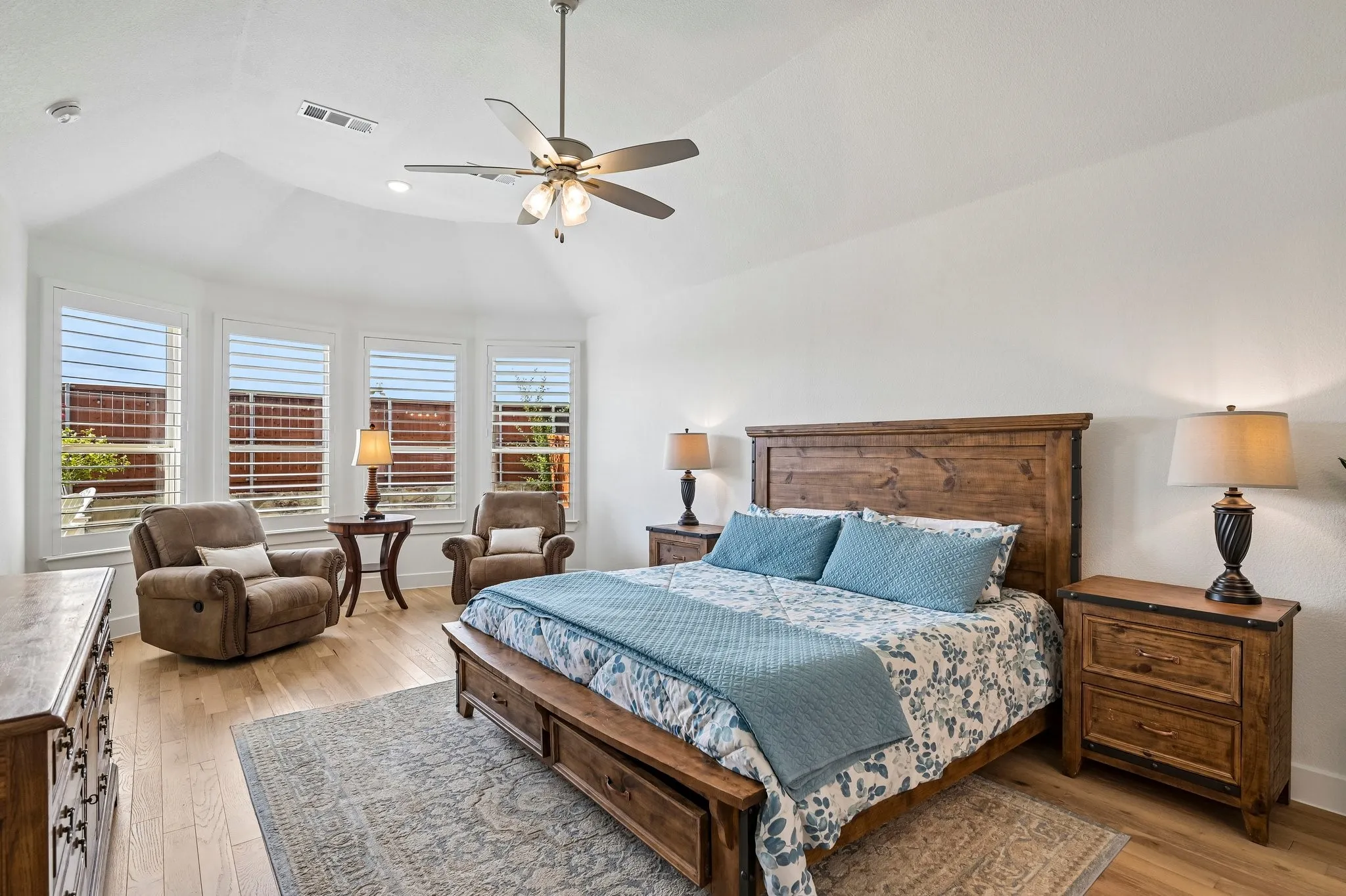 Vaulted ceiling featuring a ceiling fan, bay windows with plantation shutters, and wood-finish flooring