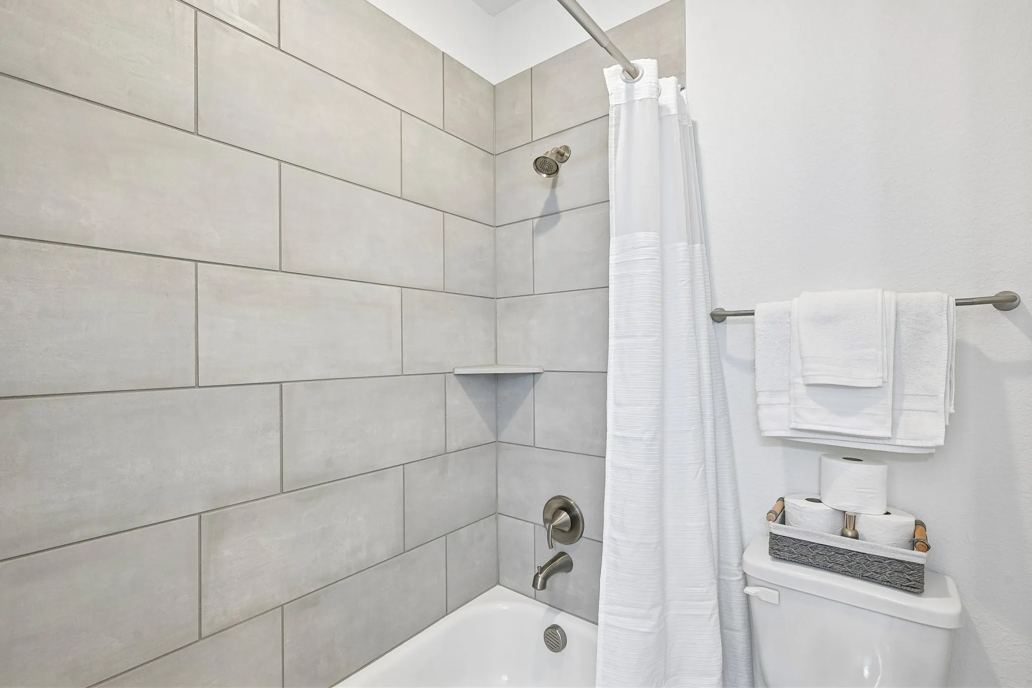Bathtub with subway tile surround, integrated shower shelf, and brushed nickel fixtures