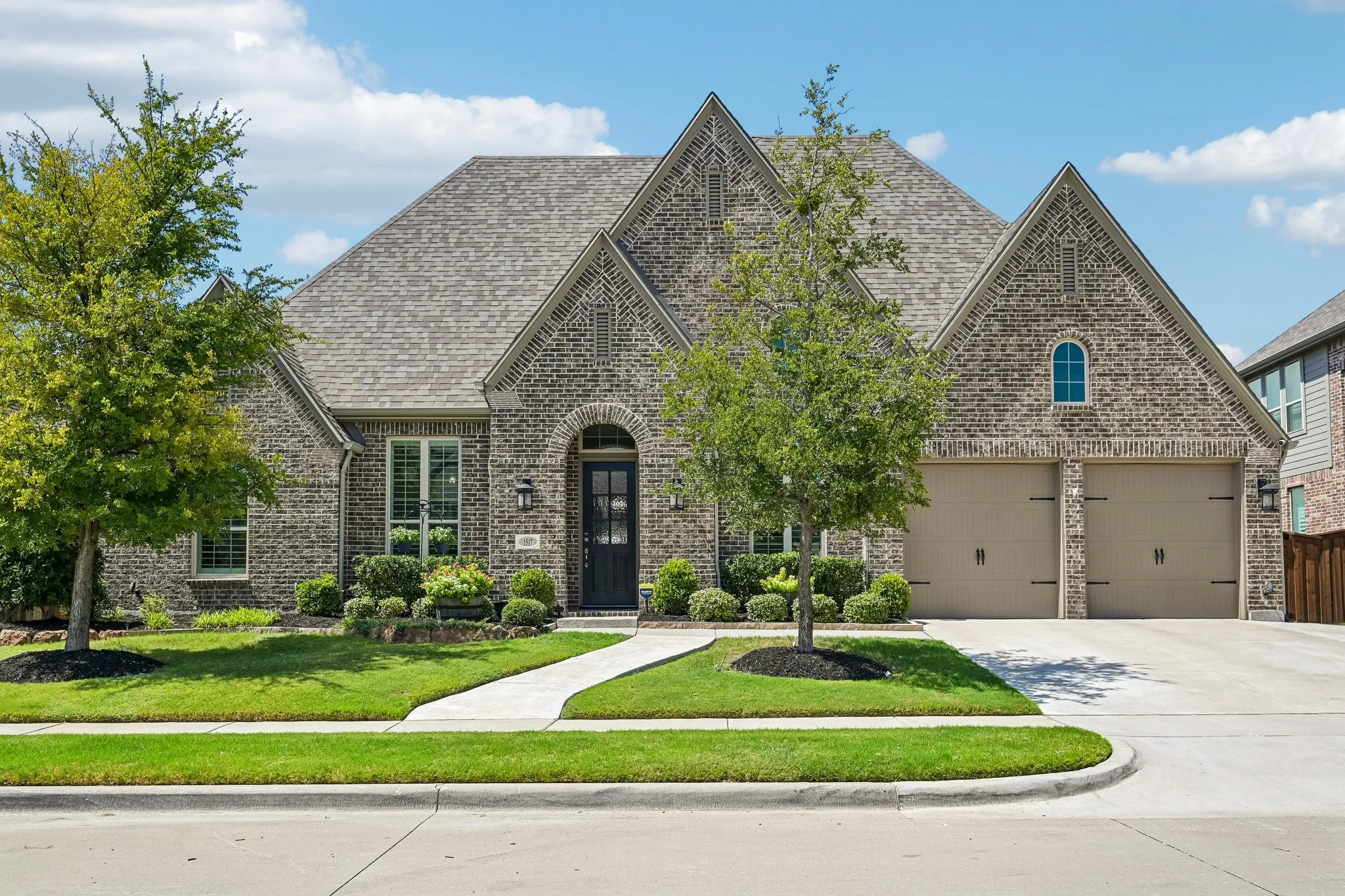 Brick facade with gabled roofline, arched entry, multiple windows with shutters, and an attached two-car garage