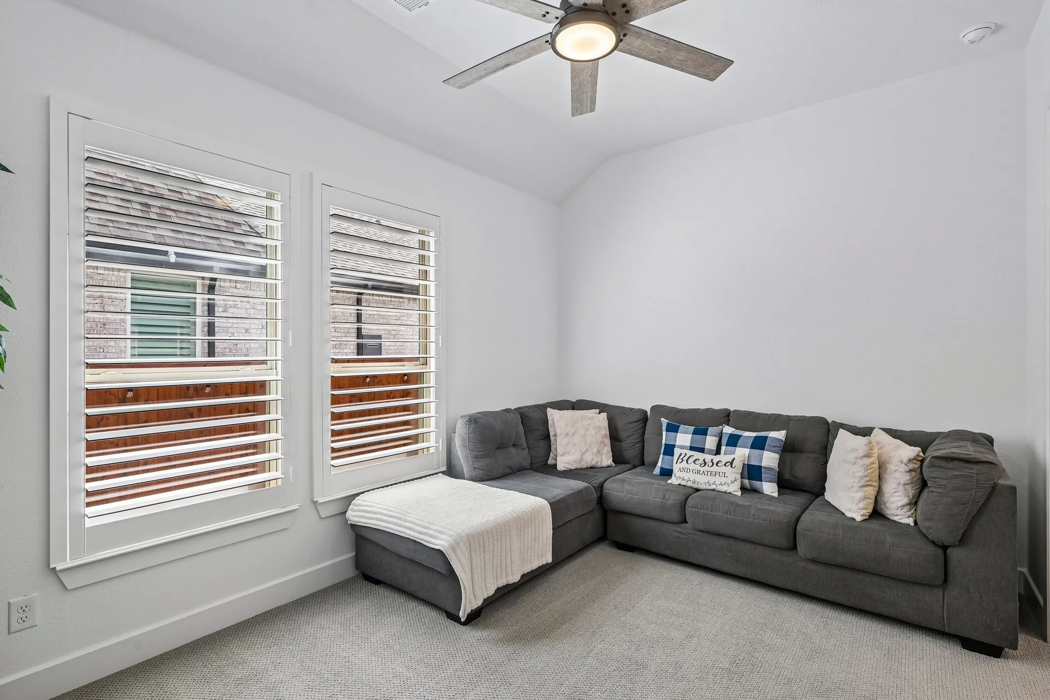 Two windows with plantation shutters, vaulted ceiling, and a ceiling fan with integrated lighting