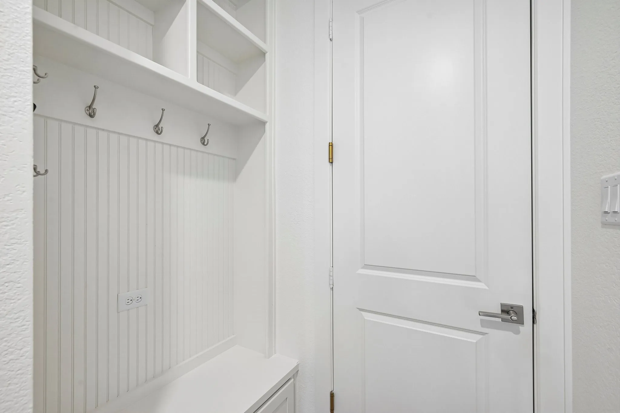 Built-in storage bench with beadboard backing, overhead shelving, and multiple coat hooks