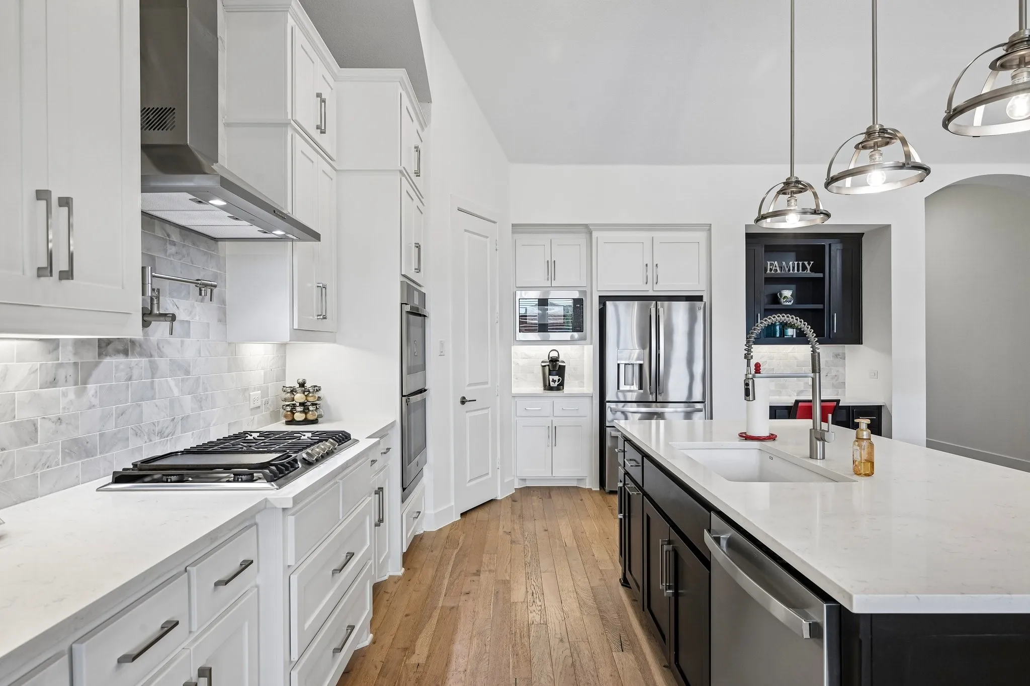 Spacious kitchen featuring white cabinetry, light-toned countertops, stainless steel appliances, a gas range, and wood-finish flooring