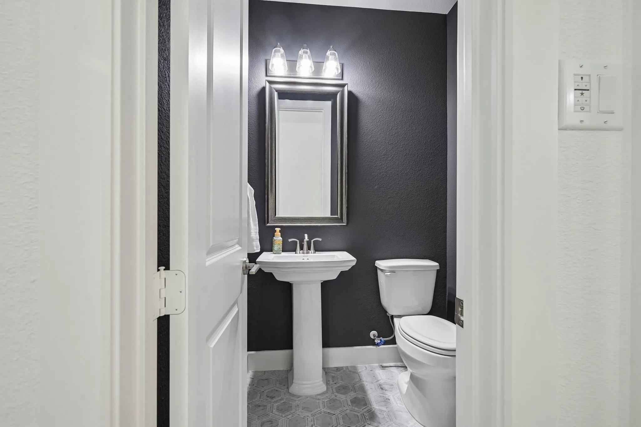 Pedestal sink with chrome faucet, hexagonal floor tiling, and dark accent wall
