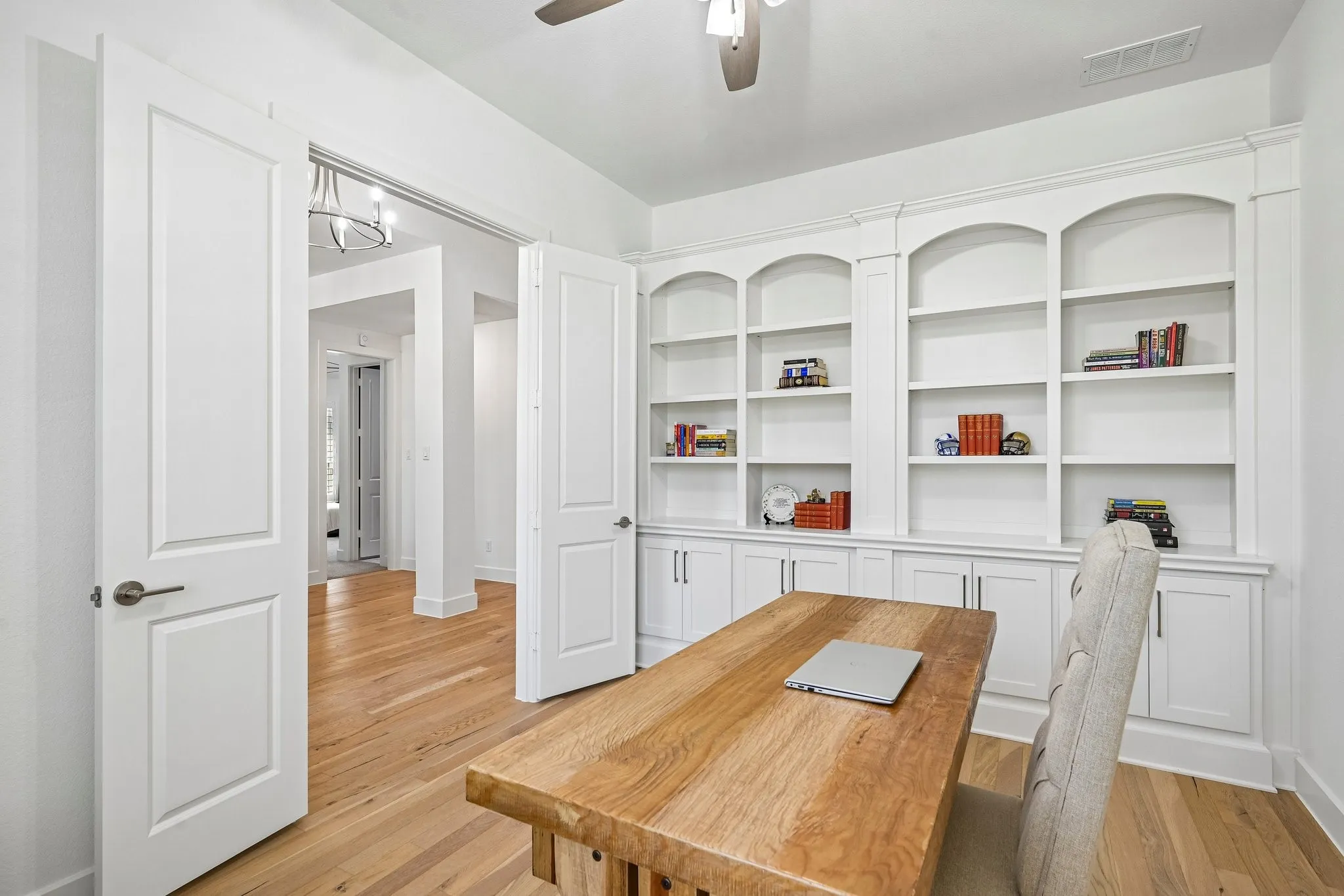 Built-in shelving with arched accents, integrated cabinetry, wood-finish flooring, and double pocket doors
