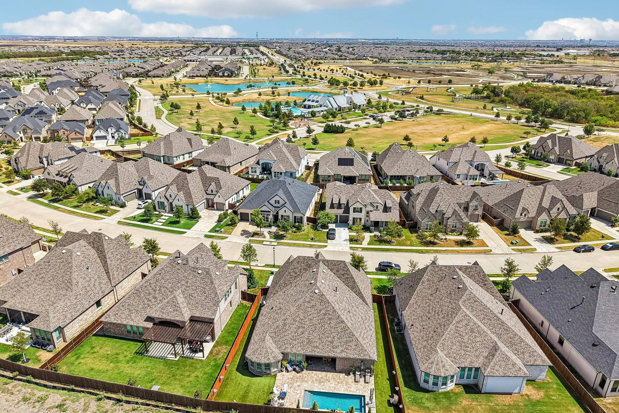 Expansive residential community featuring a variety of architectural styles, numerous properties with pitched shingle roofs, and a prominent backyard with a swimming pool and patio structure