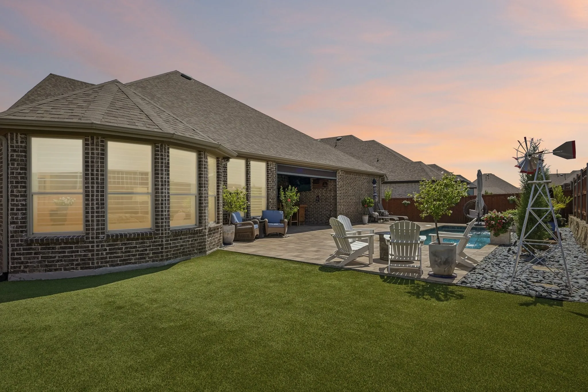 Brick exterior with bay windows, paver patio, in-ground swimming pool, and artificial turf