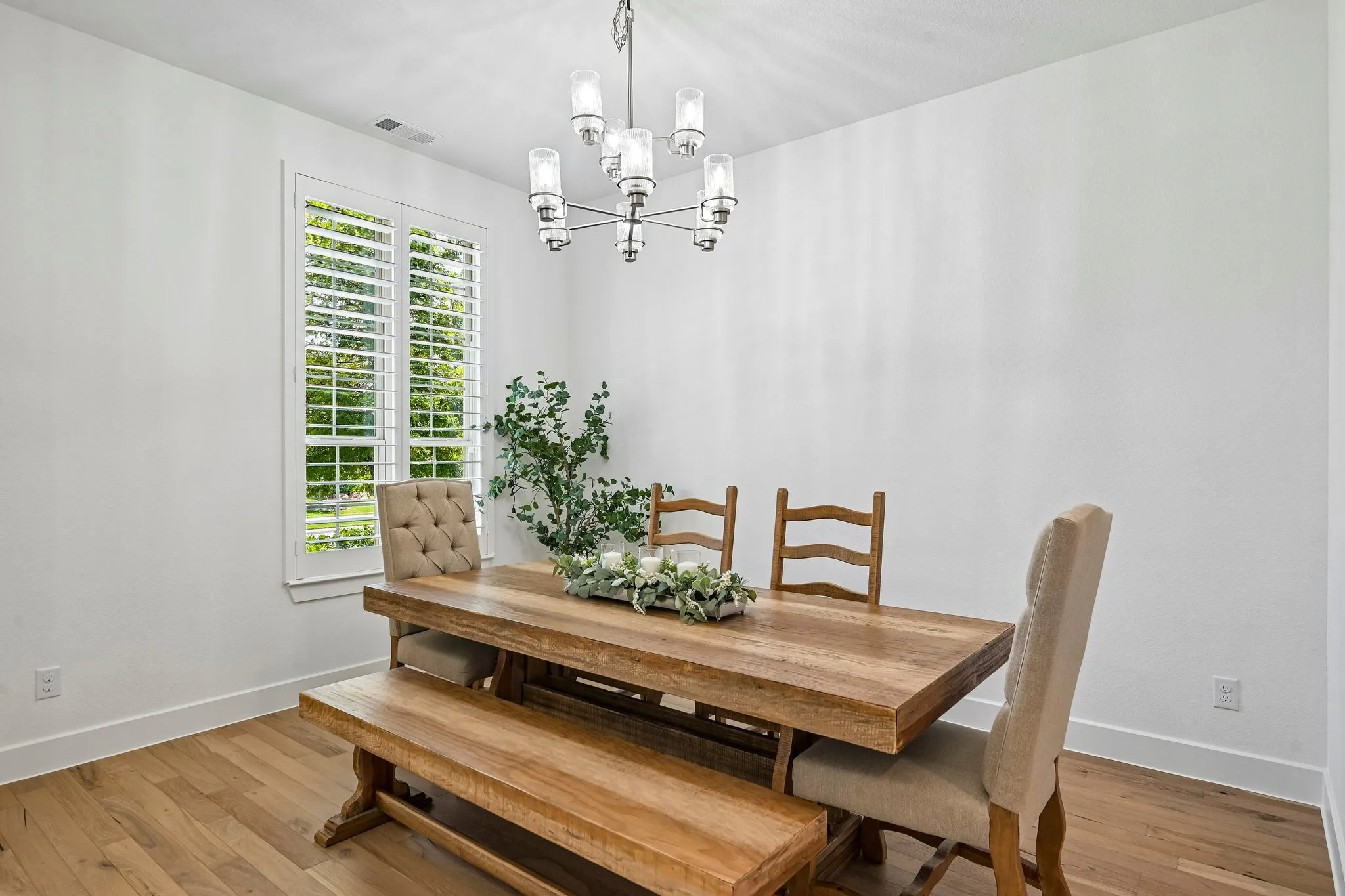 Wood flooring, white walls, window with white plantation shutters, and a multi-light chandelier