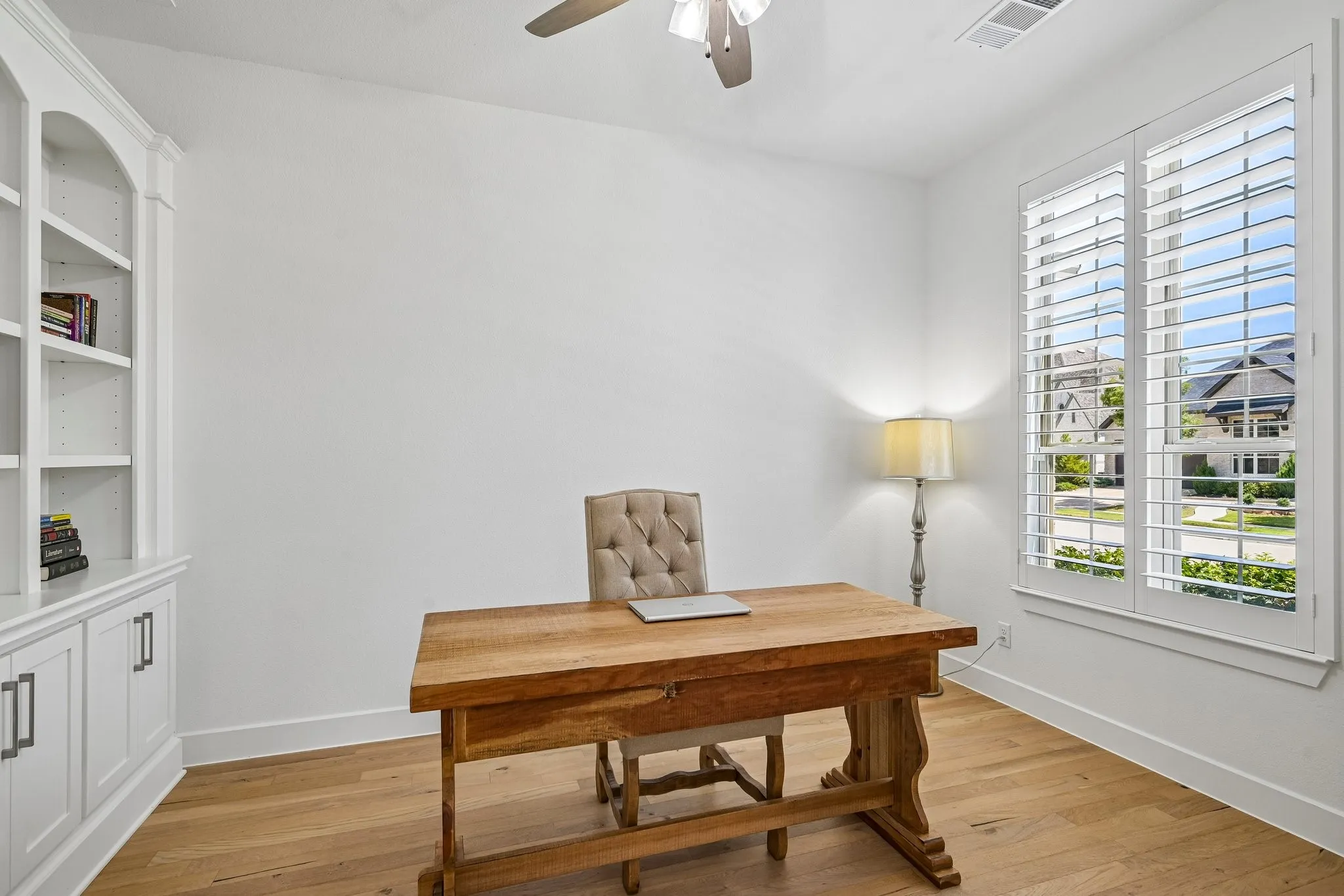 Built-in white cabinetry, hardwood flooring, ceiling fan, and white window shutters