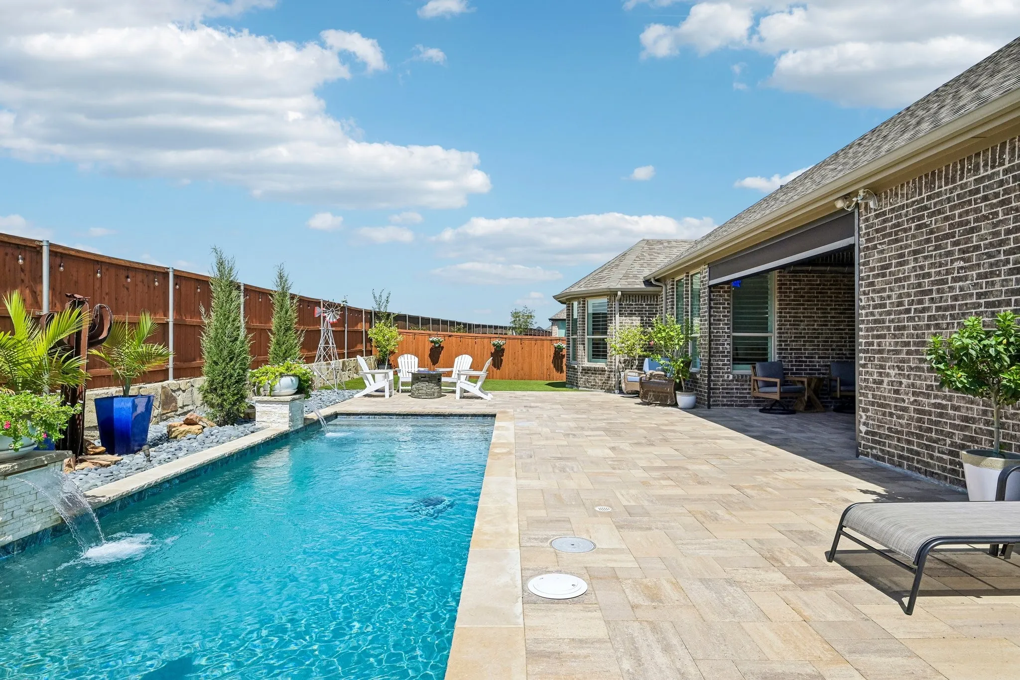 Pool with water feature, expansive paver patio, brick exterior, and recently stained wood fencing