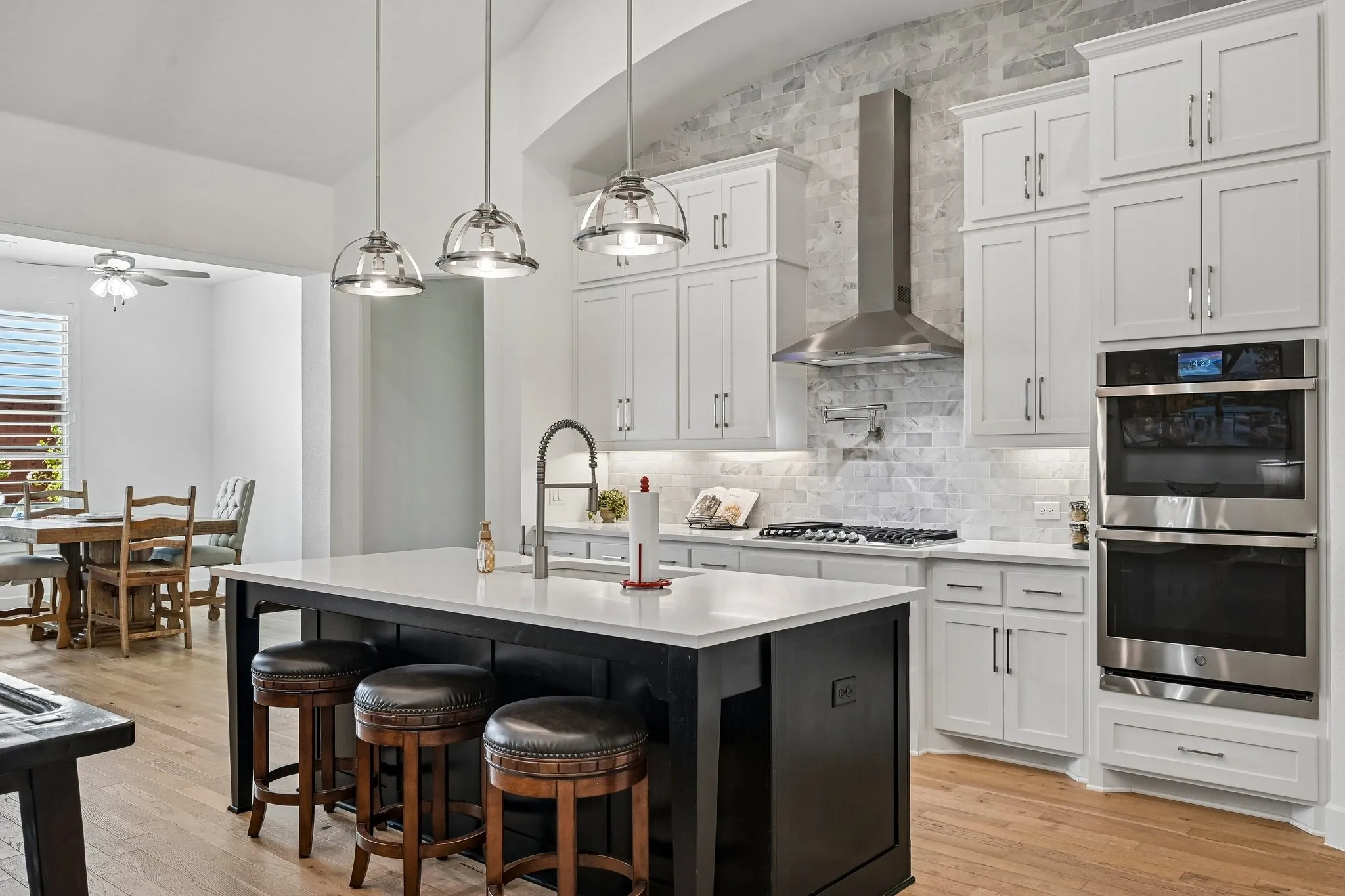 Kitchen with an expansive island featuring a white countertop and built-in sink, white shaker cabinetry, stainless steel appliances, and a full-height stone tile backsplash