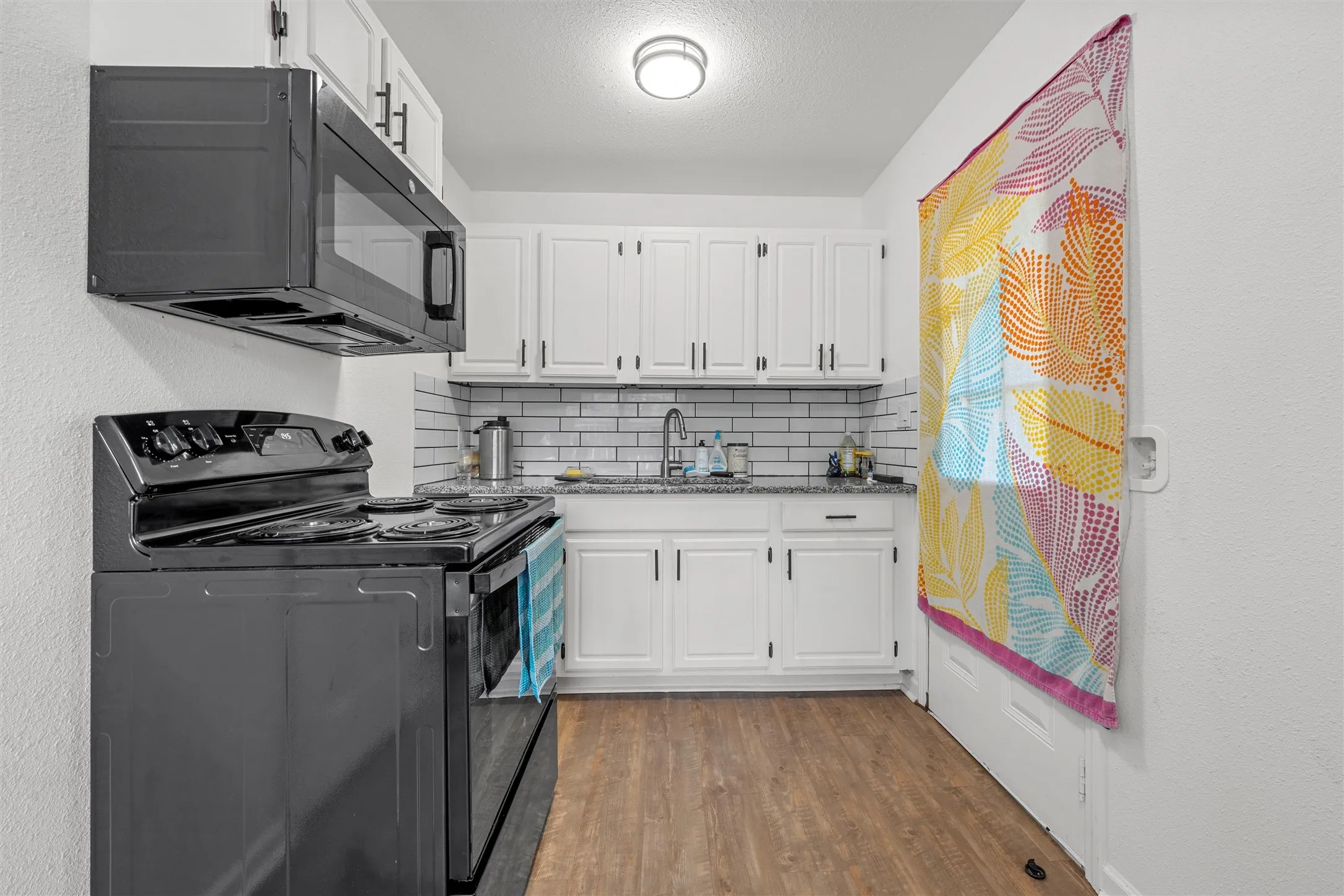 Kitchen featuring wood-finish flooring, white cabinetry with dark hardware, subway tile backsplash, and a built-in microwave