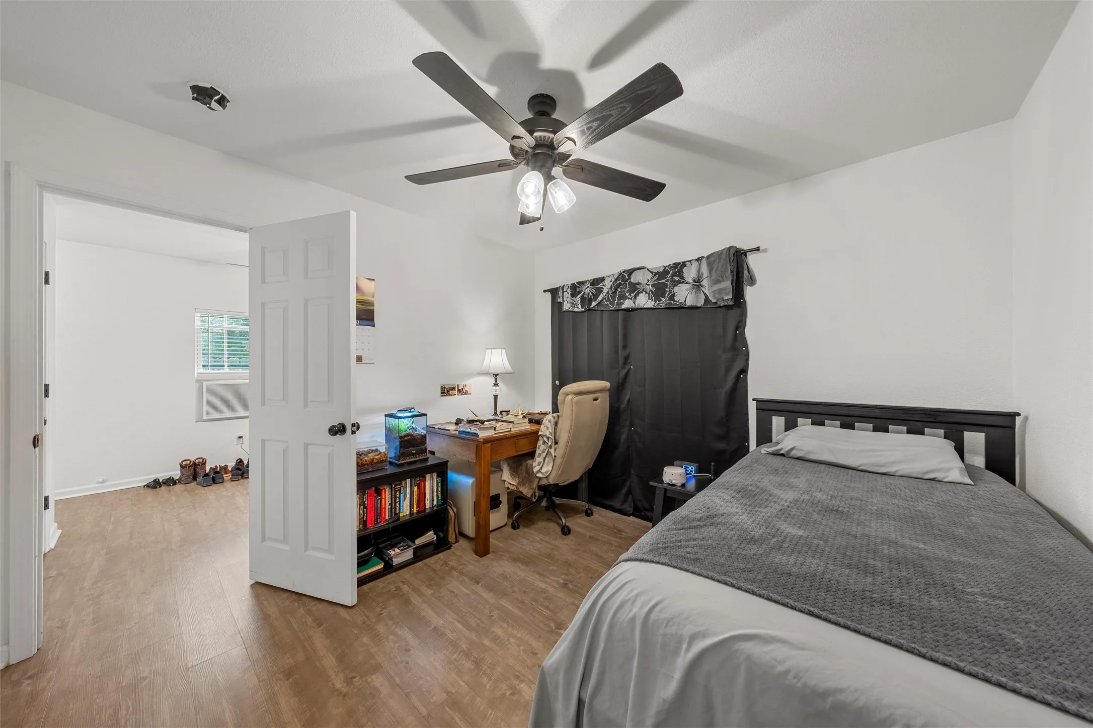 White interior walls, wood-finish flooring, ceiling fan with integrated lighting, window with blinds, and a paneled interior door