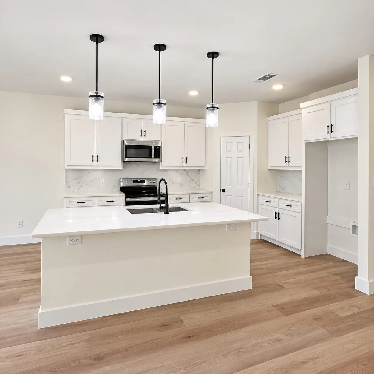 Kitchen featuring a central island with a sink, white cabinetry, integrated stainless steel microwave, black hardware, and wood-finish flooring