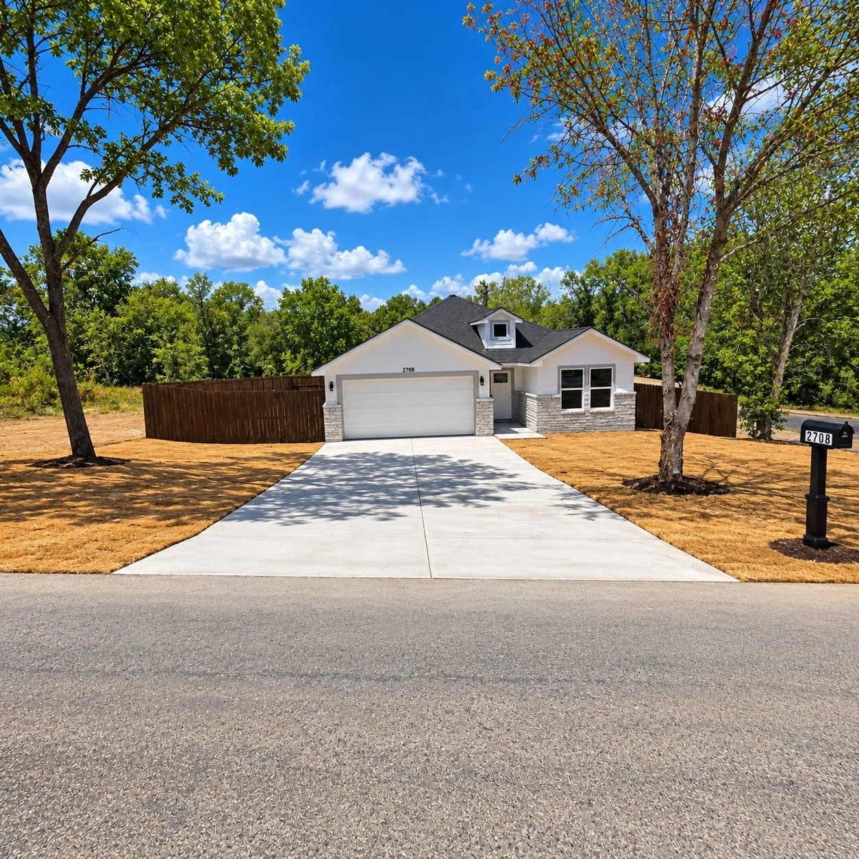 White exterior with stone accents, black roof, attached two-car garage, and concrete driveway