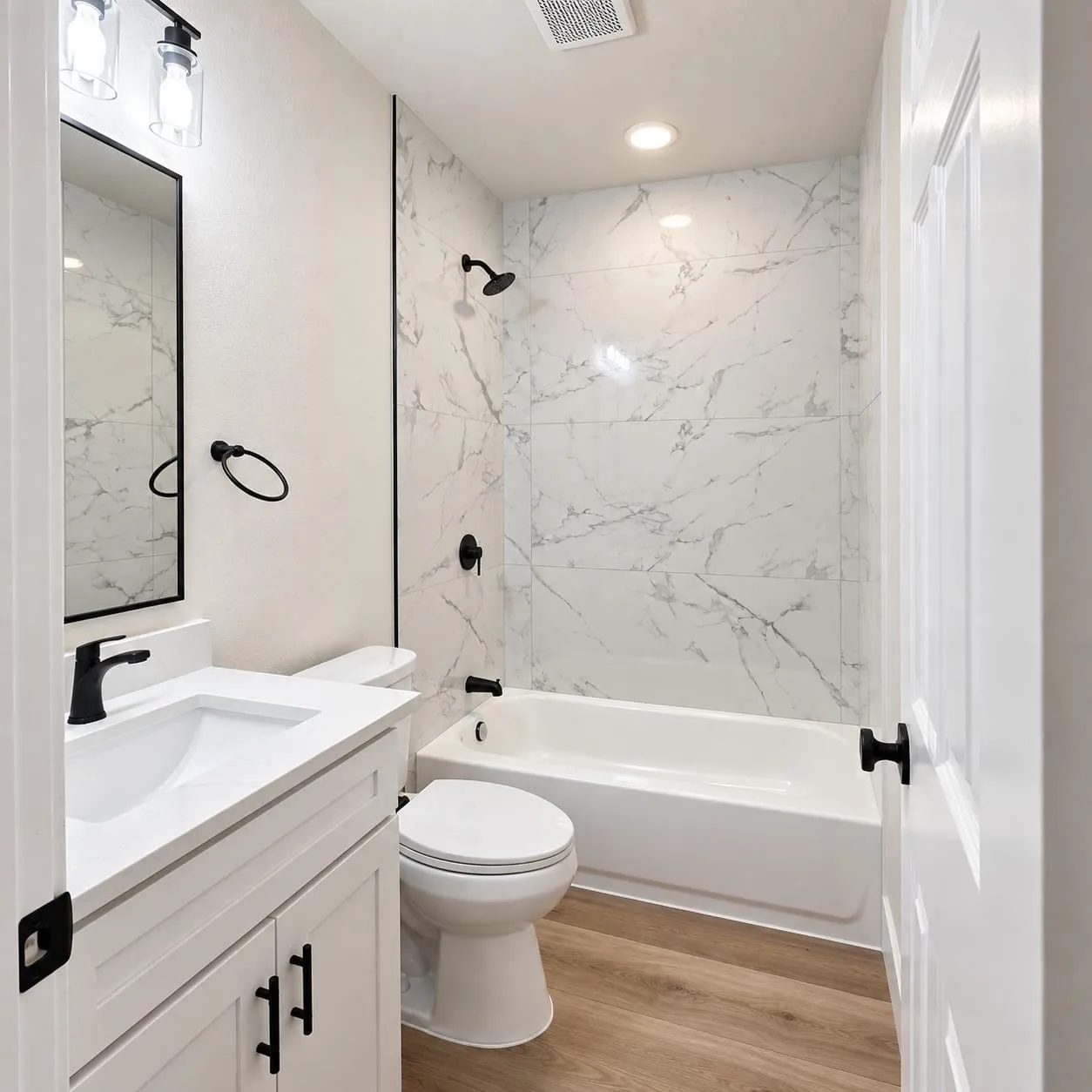 White vanity with an integrated sink, black hardware, black-framed mirror, and a tiled shower/tub combination