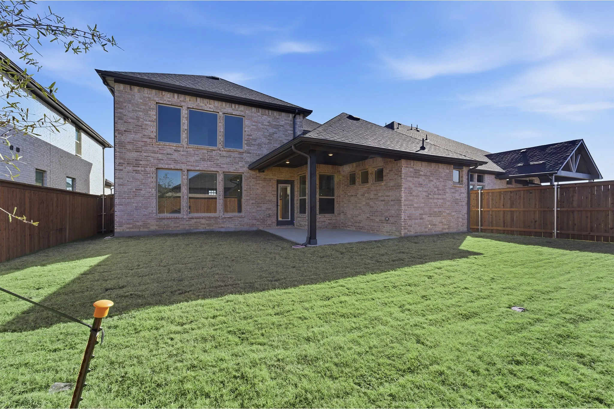 Expansive backyard featuring a manicured lawn, full privacy fencing, and a covered patio