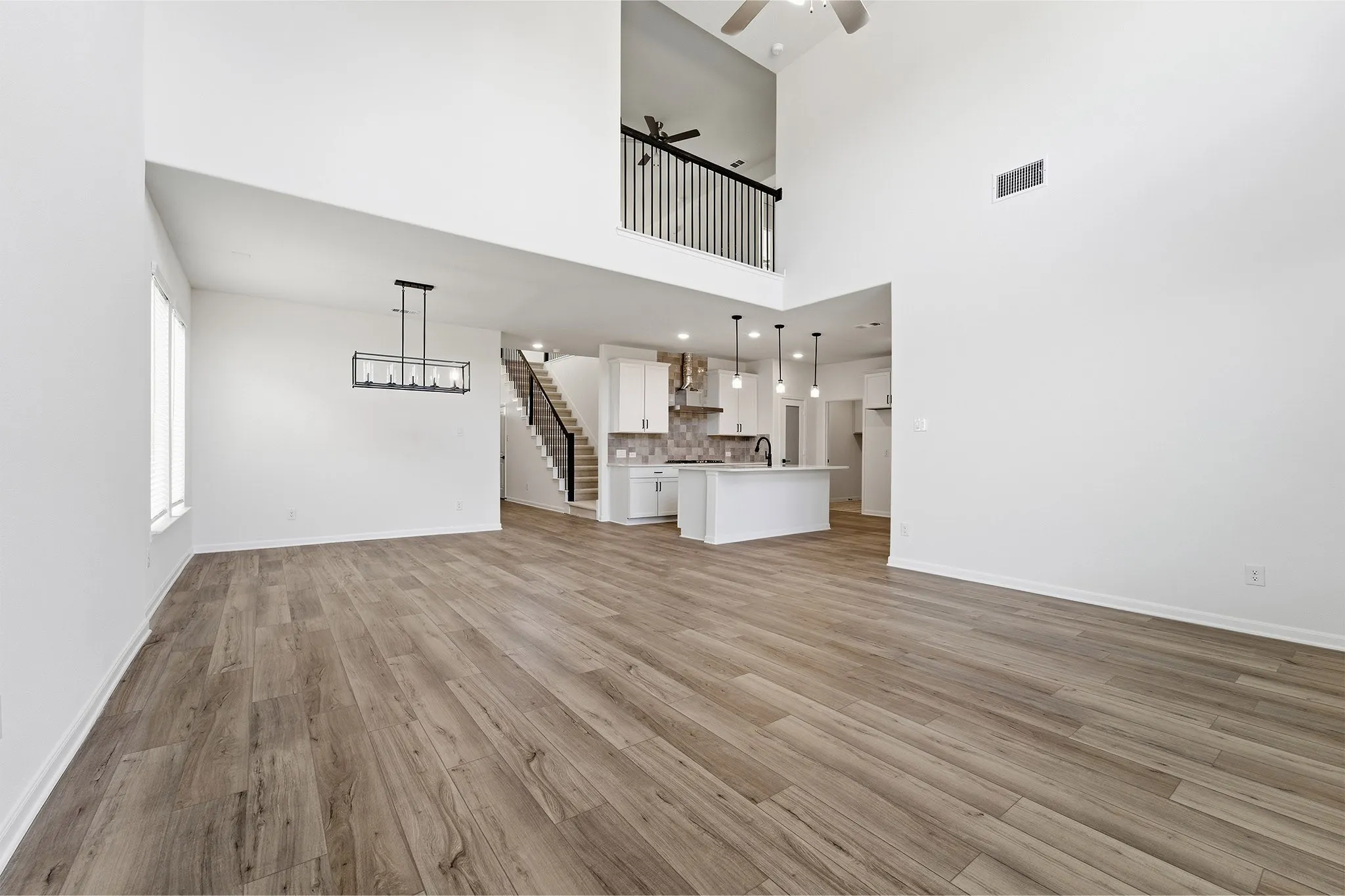 Wood-finish flooring throughout, two-story ceiling, contemporary chandelier, kitchen island with pendant lighting, and an open loft with iron railing